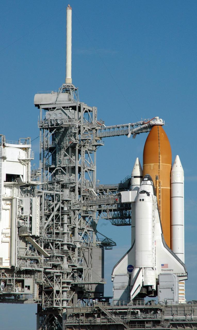 KENNEDY SPACE CENTER, FLA. --   Under a clear blue sky, Space Shuttle Discovery is ready for launch of mission STS-116 from Launch Pad 39B.  Atop the fixed service structure at left looms the 80-foot-high lightning mast, part of the lightning protection system on the pad.  Beneath Discovery's wings are the tail masts, which provide several umbilical connections to the orbiter, including a liquid-oxygen line through one and a liquid-hydrogen line through another. Seen above the golden external tank is the vent hood (known as the "beanie cap") at the end of the gaseous oxygen vent arm, extending from the FSS. Vapors are created as the liquid oxygen in the external tank boil off. The hood vents the gaseous oxygen vapors away from the space shuttle vehicle. Below it, also extending toward Discovery from the FSS, is the orbiter access arm with the White Room at the end. The crew gains access into the orbiter through the White Room.  Discovery is scheduled to launch on mission STS-116 at 9:35 p.m. today.  On the mission, the crew will deliver truss segment, P5, to the International Space Station and begin the intricate process of reconfiguring and redistributing the power generated by two pairs of U.S. solar arrays. The P5 will be mated to the P4 truss that was delivered and attached during the STS-115 mission in September. Photo credit: NASA/Ken Thornsley