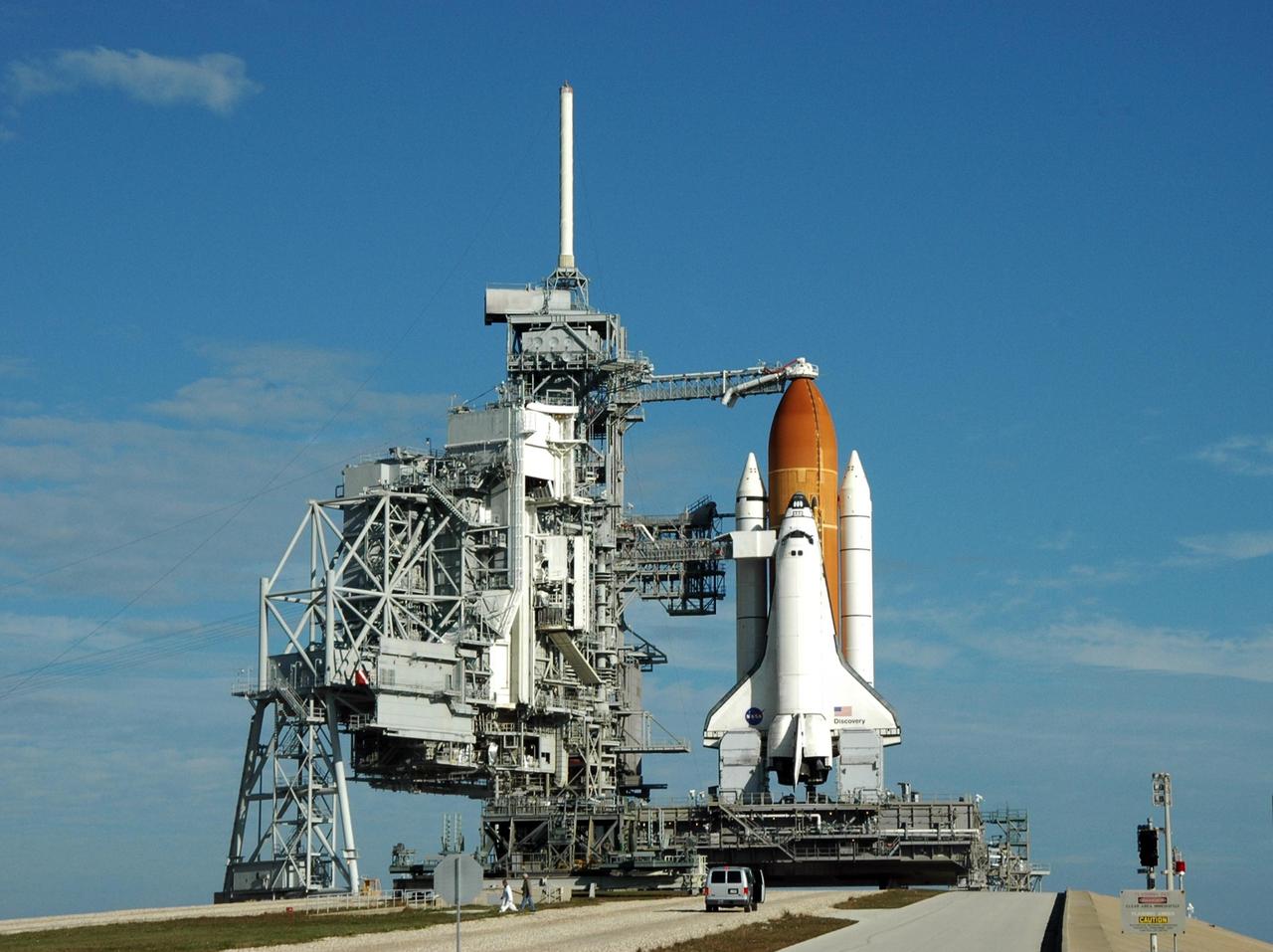KENNEDY SPACE CENTER, FLA. --    Under a blue sky streaked with clouds, Launch Pad 39B holds Space Shuttle Discovery, ready for launch of mission STS-116.  At the far left is the rotating service structure, rolled back after midnight in preparation for launch.  Next to Discovery is the fixed service structure, with the 80-foot-high lightning mast on top, part of the lightning protection system on the pad. Beneath Discovery's wings are the tail masts, which provide several umbilical connections to the orbiter, including a liquid-oxygen line through one and a liquid-hydrogen line through another.  Seen above the golden external tank is the vent hood (known as the "beanie cap") at the end of the gaseous oxygen vent arm, extending from the FSS. Vapors are created as the liquid oxygen in the external tank boil off. The hood vents the gaseous oxygen vapors away from the space shuttle vehicle. Below it, also extending toward Discovery from the FSS, is the orbiter access arm with the White Room at the end. The crew gains access into the orbiter through the White Room.  Discovery is scheduled to launch on mission STS-116 at 9:35 p.m. today.  On the mission, the crew will deliver truss segment, P5, to the International Space Station and begin the intricate process of reconfiguring and redistributing the power generated by two pairs of U.S. solar arrays. The P5 will be mated to the P4 truss that was delivered and attached during the STS-115 mission in September. Photo credit: NASA/Ken Thornsley