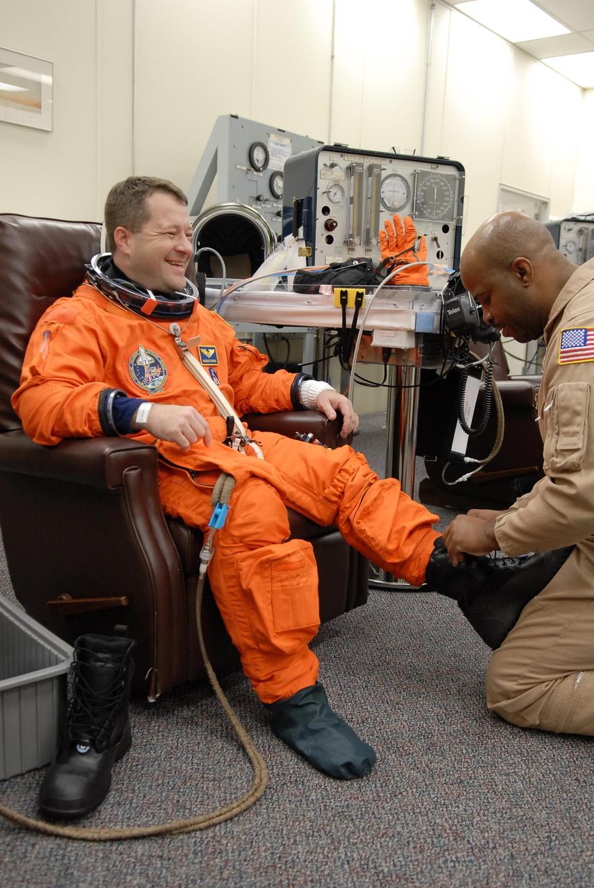 KENNEDY SPACE CENTER, FLA. -- The crew members of mission STS-116 are suiting up for launch at 9:35 p.m. EST from Launch Pad 39B aboard Space Shuttle Discovery. Pictured here is Mission Specialist Nicholas Patrick, who will be making his first shuttle flight, being helped with his boot. This is Discovery's 33rd mission and the first night launch since 2003. The 20th shuttle mission to the International Space Station, STS-116 carries another truss segment, P5. It will serve as a spacer, mated to the P4 truss that was attached in September. After installing the P5, the crew will reconfigure and redistribute the power generated by two pairs of U.S. solar arrays. Landing is expected Dec. 19 at KSC. Photo credit: NASA/Kim Shiflett