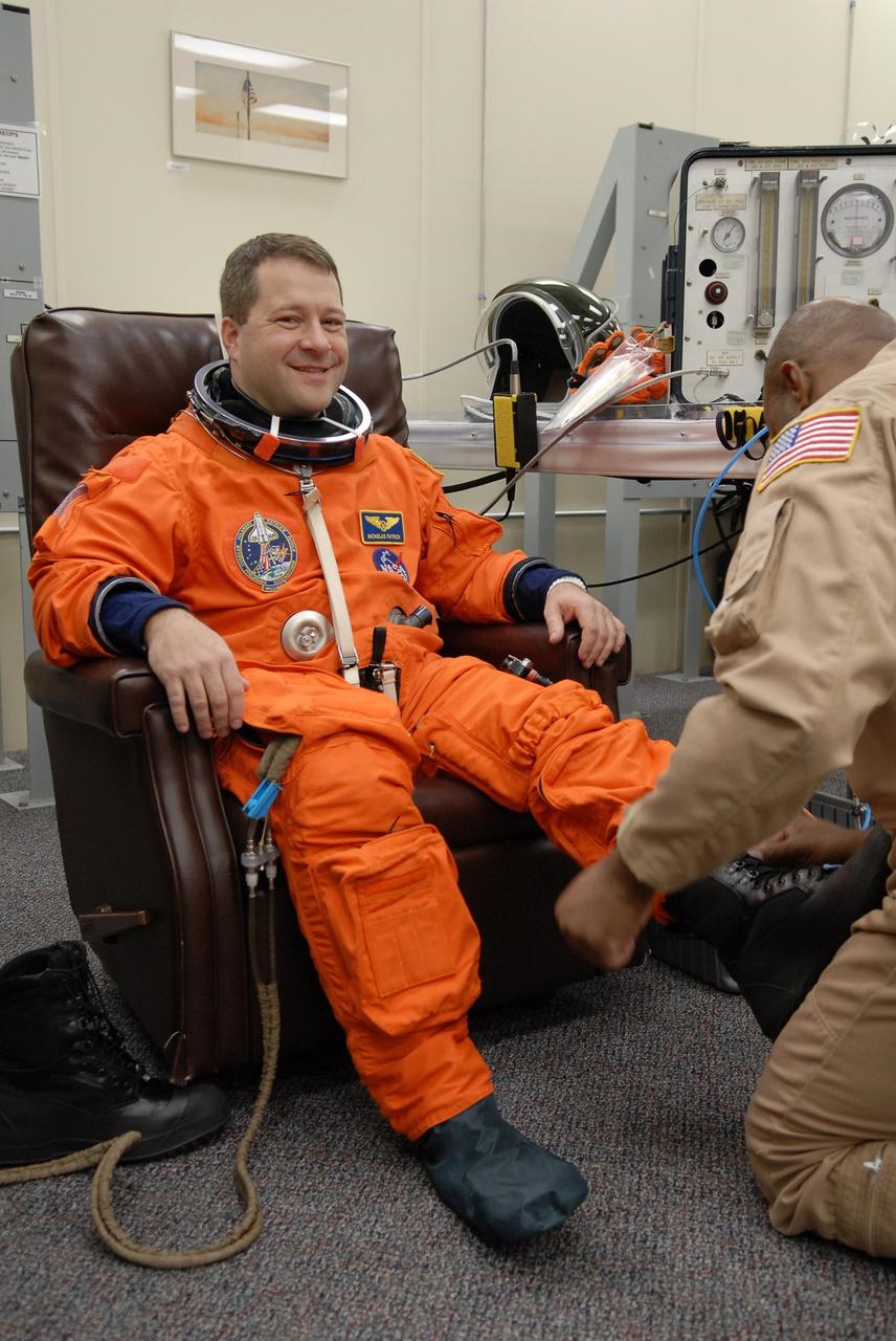 KENNEDY SPACE CENTER, FLA. --   The crew members of mission STS-116 are suiting up for a second launch attempt at 8:47 p.m. EST from Launch Pad 39B aboard Space Shuttle Discovery.   Pictured here is Mission Specialist Nicholas Patrick, who will be making his first shuttle flight, being helped with his boot. The first launch attempt of STS-116 on Dec. 7 was postponed due a low cloud ceiling over Kennedy Space Center. This is Discovery's 33rd mission and the first night launch since 2002.   The 20th shuttle mission to the International Space Station, STS-116 carries another truss segment, P5. It will serve as a spacer, mated to the P4 truss that was attached in September.  After installing the P5, the crew will reconfigure and redistribute the power generated by two pairs of U.S. solar arrays. Landing is expected Dec. 19 at KSC.   Photo credit: NASA/Kim Shiflett
