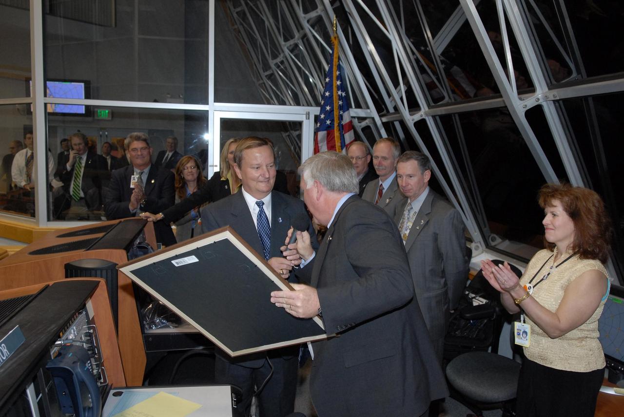 KENNEDY SPACE CENTER, FLA. --  In the firing room at the Launch Control Center, Shuttle Launch Director Mike Leinbach presents a memento of the night's successful launch of Space Shuttle Discovery to Kennedy Space Center Director Jim Kennedy, who is retiring in January.   Behind Leinbach and Kennedy are, left to right, Deputy Director Bill Parsons, External Relations Director Lisa Malone, NASA Flow Director for Discovery Stephanie Stilson, NASA KSC News Chief Bruce Buckingham, Associate Administrator for Space Operations Mission William Gerstenmaier and NASA  Administrator Mike Griffin and his wife, Becky.   This was the second launch attempt for mission STS-116.  The first launch attempt on Dec. 7 was postponed due a low cloud ceiling over Kennedy Space Center. This is Discovery's 33rd mission and the first night launch since 2002.   The 20th shuttle mission to the International Space Station, STS-116 carries another truss segment, P5. It will serve as a spacer, mated to the P4 truss that was attached in September.  After installing the P5, the crew will reconfigure and redistribute the power generated by two pairs of U.S. solar arrays. Landing is expected Dec. 21 at KSC.   Photo credit: NASA/Kim Shiflett