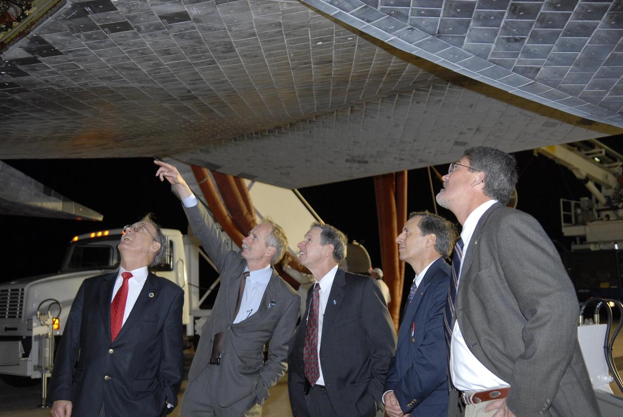 KENNEDY SPACE CENTER, FLA. --  Sigmar Wittig, head of the DLR, the German Space Agency; Bill Gerstenmaier, NASA associate administrator for Space Operations; Mike Griffin, NASA administrator; Michel Tognini, head of the European Astronaut Center; and Bill Parsons, Kennedy Space Center deputy director, examine the thermal protection system tiles beneath Space Shuttle Discovery following the landing of mission STS-116 on Runway 15 at NASA Kennedy Space Center's Shuttle Landing Facility. During the STS-116 mission, three spacewalks attached the P5 integrated truss structure to the station, and completed the rewiring of the orbiting laboratory's power system.  A fourth spacewalk retracted a stubborn solar array. Main gear touchdown was at 5:32 p.m. EST. Nose gear touchdown was at 5:32:12 p.m. and wheel stop was at 5:32:52 p.m.  At touchdown -- nominally about 2,500 ft. beyond the runway threshold -- the orbiter is traveling at a speed ranging from 213 to 226 mph. Discovery traveled 5,330,000 miles, landing on orbit 204. Mission elapsed time was 12 days, 20 hours, 44 minutes and 16 seconds. This is the 64th landing at KSC. Photo credit: NASA/Kim Shiflett