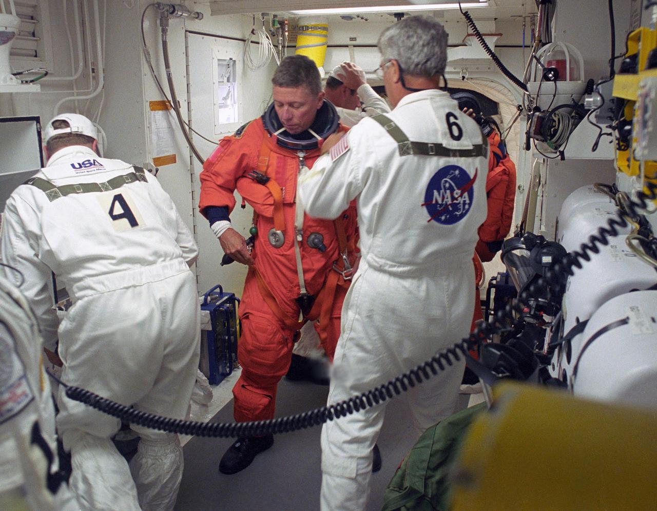 KENNEDY SPACE CENTER, FLA. -    In the White Room on Launch Pad 39B, STS-121 Mission Specialist Michael Fossum gets help from the Closeout Crew with final preparations on his launch suit before entering Discovery.  Situated on the end of the orbiter access arm, the White Room provides access into the orbiter on the pad.  The crew is preparing for the third launch attempt in four days; previous attempts were scrubbed due to weather concerns.  During the 12-day mission, the STS-121 crew will test new equipment and procedures to improve shuttle safety, as well as deliver supplies and make repairs to the International Space Station. The launch of Space Shuttle Discovery on mission STS-121 is the 115th shuttle flight and the 18th U.S. flight to the International Space Station.