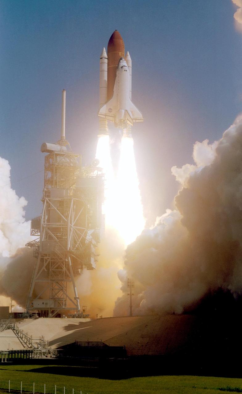 KENNEDY SPACE CENTER, FLA. -   Twin columns of fire propel Space Shuttle Atlantis into a clear blue sky after liftoff from Launch Pad 39B.  At left is the fixed service structure, topped by the lightning mast.  Clouds of smoke and steam nearly obscure the pad.  Atlantis is heading for a rendezvous with the International Space Station on mission STS-115.  Liftoff was on-time at 11:14:55 a.m. EDT. After several launch attempts were scrubbed due to weather and technical concerns, this launch was executed perfectly. Mission STS-115 is the 116th space shuttle flight, the 27th flight for orbiter Atlantis, and the 19th U.S. flight to the International Space Station.  During the mission, Atlantis' astronauts will deliver and install the 17.5-ton, bus-sized P3/P4 integrated truss segment on the station. The girder-like truss includes a set of giant solar arrays, batteries and associated electronics and will provide one-fourth of the total power-generation capability for the completed station. STS-115 is scheduled to last 11 days with a planned landing at KSC