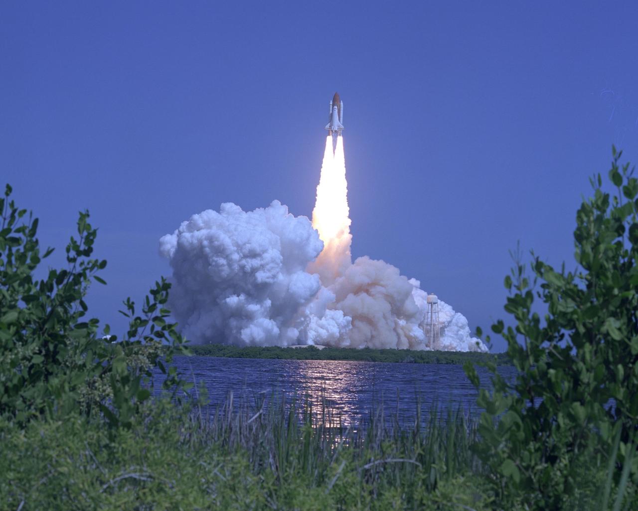 KENNEDY SPACE CENTER, FLA. -   Space Shuttle Atlantis hurtles toward space, propelled by twin columns of fire from the solid rocket boosters, which are captured in the reflection on the water.  The resulting clouds of smoke and steam billow across Launch Pad 39B and upward, obscuring the service structures on the pad.   Atlantis is heading for a rendezvous with the International Space Station on mission STS-115.  Liftoff was on-time at 11:14:55 a.m. EDT. After several launch attempts were scrubbed due to weather and technical concerns, this launch was executed perfectly. Mission STS-115 is the 116th space shuttle flight, the 27th flight for orbiter Atlantis, and the 19th U.S. flight to the International Space Station.  During the mission, Atlantis' astronauts will deliver and install the 17.5-ton, bus-sized P3/P4 integrated truss segment on the station. The girder-like truss includes a set of giant solar arrays, batteries and associated electronics and will provide one-fourth of the total power-generation capability for the completed station. STS-115 is scheduled to last 11 days with a planned landing at KSC