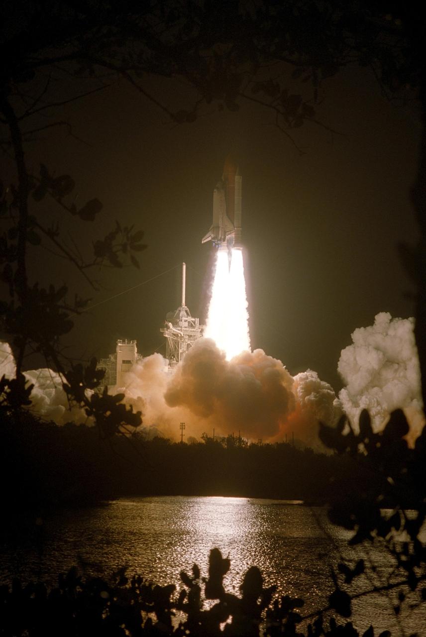 KENNEDY SPACE CENTER, FLA. --    Viewed through the leaves of a tree in the foreground, the fiery liftoff of Space Shuttle Discovery on mission STS-116 lights up the nearby water.  Liftoff occurred on time at 8:47 p.m. EST.  This was the second launch attempt for mission STS-116.  The first launch attempt on Dec. 7 was postponed due a low cloud ceiling over Kennedy Space Center. This is Discovery's 33rd mission and the first night launch since 2002.   The 20th shuttle mission to the International Space Station, STS-116 carries another truss segment, P5. It will serve as a spacer, mated to the P4 truss that was attached in September.  After installing the P5, the crew will reconfigure and redistribute the power generated by two pairs of U.S. solar arrays. Landing is expected Dec. 21 at KSC.   Photo credit: NASA/Sandy Joseph, Robert Murray & Chris Lynch