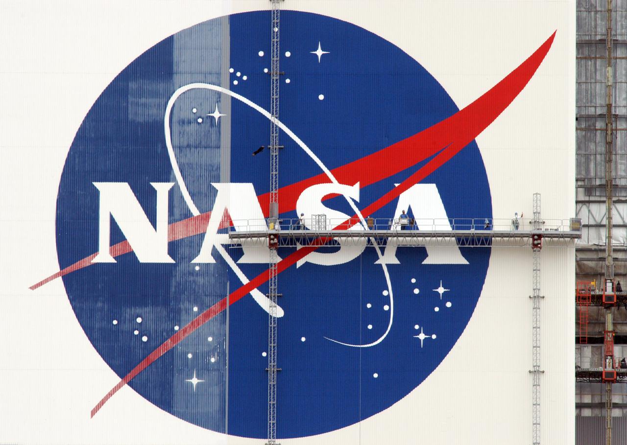 On platforms suspended from the top of the 525-foot-high VAB, workers use rollers and brushes to repaint the NASA logo on the southeast side of the Vehicle Assembly Building. Known as the "meatball," the logo measures 110 feet by 132 feet, or about 12,300 square feet. The U.S. flag is also being repainted. The flag spans an area 209 feet by 110 feet, or about 23, 437 square feet. Each stripe is 9 feet wide and each star is 6 feet in diameter. The flag and logo were last painted in 1998, honoring NASA's 40th anniversary.