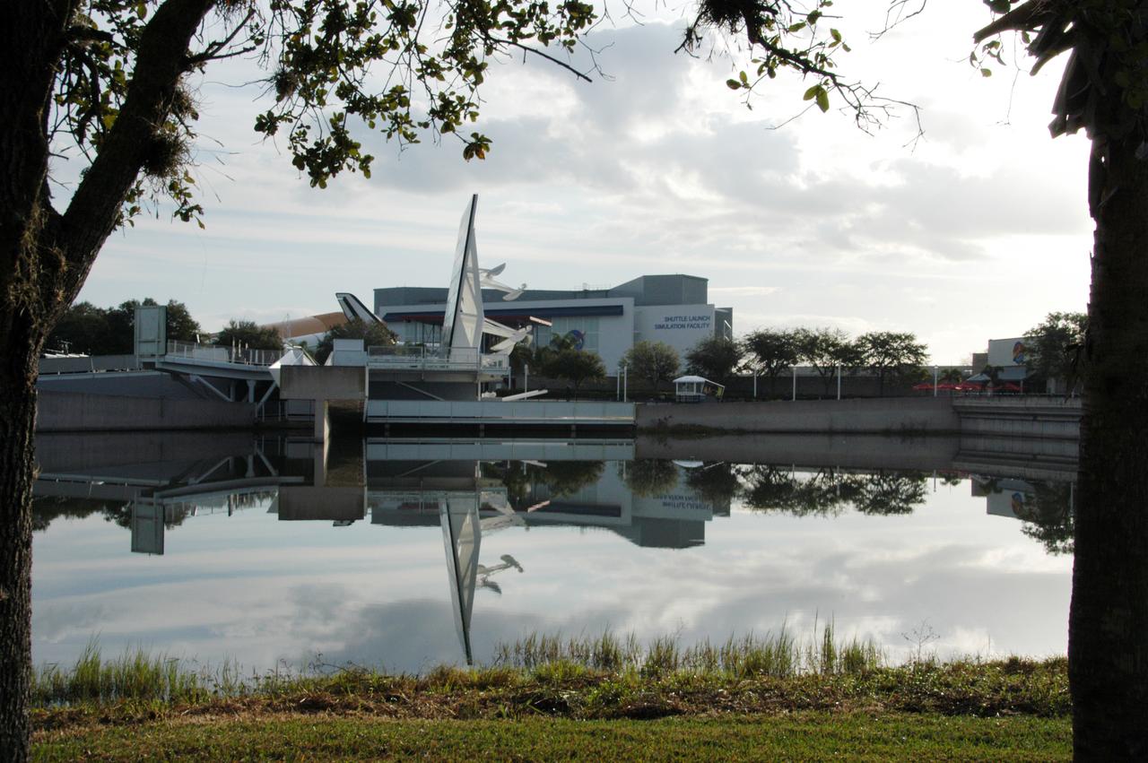 The Space Mirror Memorial, seen in profile, is reflected in the nearby lake at the KSC Visitor Complex. The memorial is the scene of a ceremony being held in remembrance of the astronauts lost in the Apollo 1 fire: Virgil "Gus" Grissom, Edward H. White II and Roger B. Chaffee. The mirror was designated as a national memorial by Congress and President George Bush in 1991 to honor fallen astronauts. Their names are emblazoned on the monument's 42-1/2-foot-high by 50-foot-wide black granite surface as if to be projected into the heavens. 