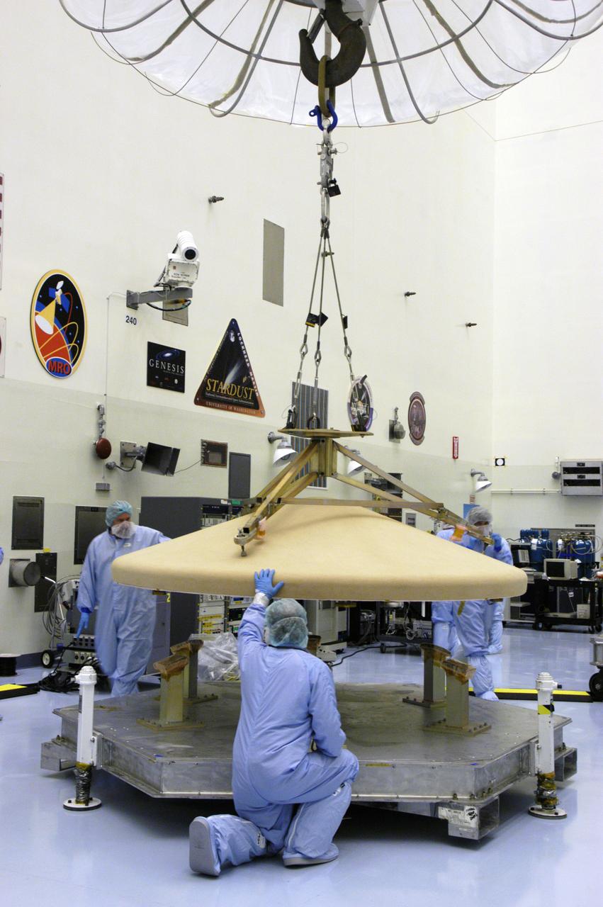 In the Payload Hazardous Servicing Facility, workers help guide the heat shield onto a platform. The heat shield was removed from the Phoenix Mars Lander spacecraft.. The Phoenix mission is the first project in NASA's first openly competed program of Mars Scout missions. Phoenix will land in icy soils near the north polar permanent ice cap of Mars and explore the history of the water in these soils and any associated rocks, while monitoring polar climate. Landing is planned in May 2008 on arctic ground where a mission currently in orbit, Mars Odyssey, has detected high concentrations of ice just beneath the top layer of soil. It will serve as NASA's first exploration of a potential modern habitat on Mars and open the door to a renewed search for carbon-bearing compounds, last attempted with NASA’s Viking missions in the 1970s. A stereo color camera and a weather station will study the surrounding environment while the other instruments check excavated soil samples for water, organic chemicals and conditions that could indicate whether the site was ever hospitable to life. Microscopes can reveal features as small as one one-thousandth the width of a human hair. Launch of Phoenix aboard a Delta II rocket is targeted for Aug. 3 from Cape Canaveral Air Force Station in Florida.