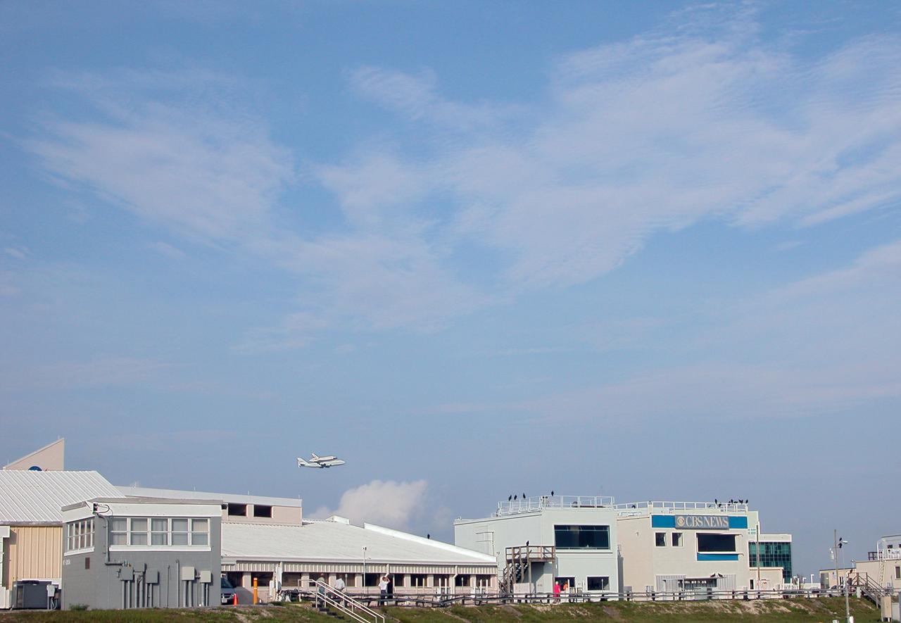 On a morning where broken clouds filled the sky of Central Florida, the shuttle carrier aircraft, or SCA, and its passenger Atlantis ease their way past the NASA News Center for a landing at the KSC Shuttle Landing Facility, known as the SLF. The aircraft is a modified Boeing 747 jetliner Atlantis landed at Edwards Air Force Base in California to end mission STS-117. The return to KSC began July 1 and took three days after stops across the country for fuel. The last stop was at Ft. Campbell in Kentucky. Weather conditions over the last leg postponed the return trip until July 3. Touchdown was at 8:27 a.m. EDT. Atlantis will be removed from the back of the SCA via the mate/demate device at the SLF. It will then be towed to the Orbiter Processing Facility to begin processing for its next launch, mission STS-122 in December. 