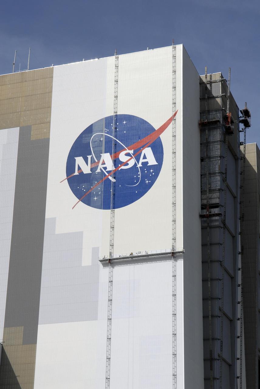 KENNEDY SPACE CENTER, FLA. --  Painters' scaffolding is seen hanging on the side of Kennedy Space Center's Vehicle Assembly Building to facilitate the repainting of the NASA logo. The American flag is also being repainted. Workers, suspended on platforms from the top of the 525-foot-high VAB, use rollers and brushes to do the painting. The flag and logo were last painted in 1998, honoring NASA's 40th anniversary. The flag spans an area 209 feet by 110 feet, or about 23,437 square feet. Each stripe is 9 feet wide and each star is 6 feet in diameter. The logo, also known as the "meatball," measures 110 feet by 132 feet, or about 12,300 square feet. Photo credit: NASA/Kim Shiflett
