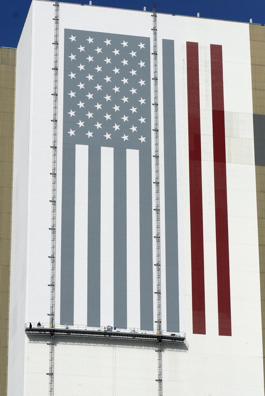 KENNEDY SPACE CENTER, FLA. --  Painters' scaffolding is seen hanging on the side of Kennedy Space Center's Vehicle Assembly Building to facilitate the repainting of the American flag.  The NASA logo is also being repainted.  Workers, suspended on platforms from the top of the 525-foot-high VAB, use rollers and brushes to do the painting. The flag and logo were last painted in 1998, honoring NASA's 40th anniversary. The flag spans an area 209 feet by 110 feet, or about 23,437 square feet. Each stripe is 9 feet wide and each star is 6 feet in diameter. The logo, also known as the "meatball," measures 110 feet by 132 feet, or about 12,300 square feet. Photo credit: NASA/Kim Shiflett