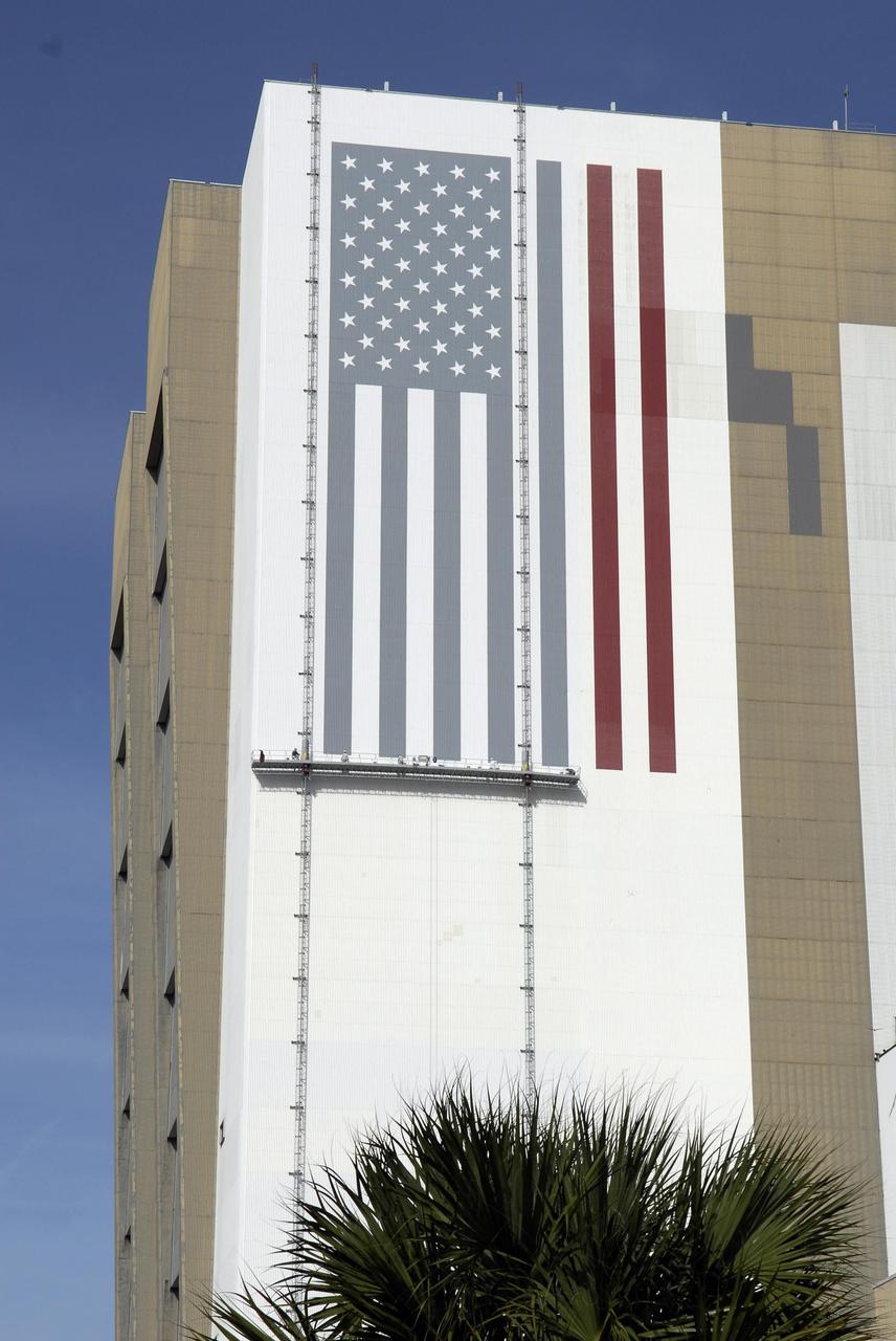 KENNEDY SPACE CENTER, FLA. --   Painters' platforms are seen hanging on the side of Kennedy Space Center's 525-foot-high Vehicle Assembly Building to facilitate the repainting of the American flag.  The NASA logo is also being repainted.  Workers use rollers and brushes to do the painting. The flag and logo were last painted in 1998, honoring NASA's 40th anniversary. The flag spans an area 209 feet by 110 feet, or about 23,437 square feet. Each stripe is 9 feet wide and each star is 6 feet in diameter. The logo, also known as the "meatball," measures 110 feet by 132 feet, or about 12,300 square feet. Photo credit: NASA/Kim Shiflett