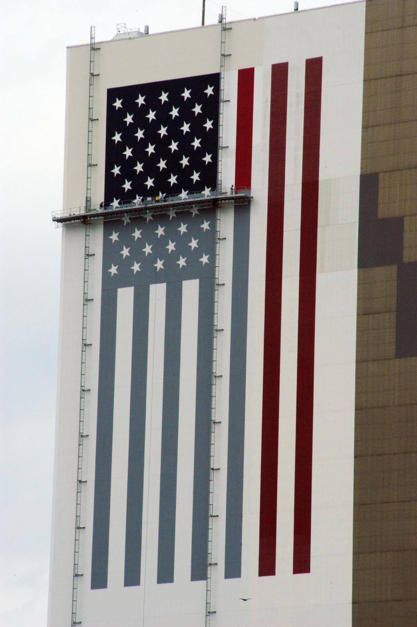 KENNEDY SPACE CENTER, FLA. --  On platforms suspended from the top of the 525-foot-high VAB, workers use rollers and brushes to repaint the U.S. flag on the southwest side of the Vehicle Assembly Building.   The flag spans an area 209 feet by 110 feet, or about 23, 437 square feet. Each stripe is 9 feet wide and each star is 6 feet in diameter. The logo is also being painted.  Known as the "meatball," the logo measures 110 feet by 132 feet, or about 12,300 square feet.  The flag and logo were last painted in 1998, honoring NASA's 40th anniversary.  Photo credit: NASA/George Shelton