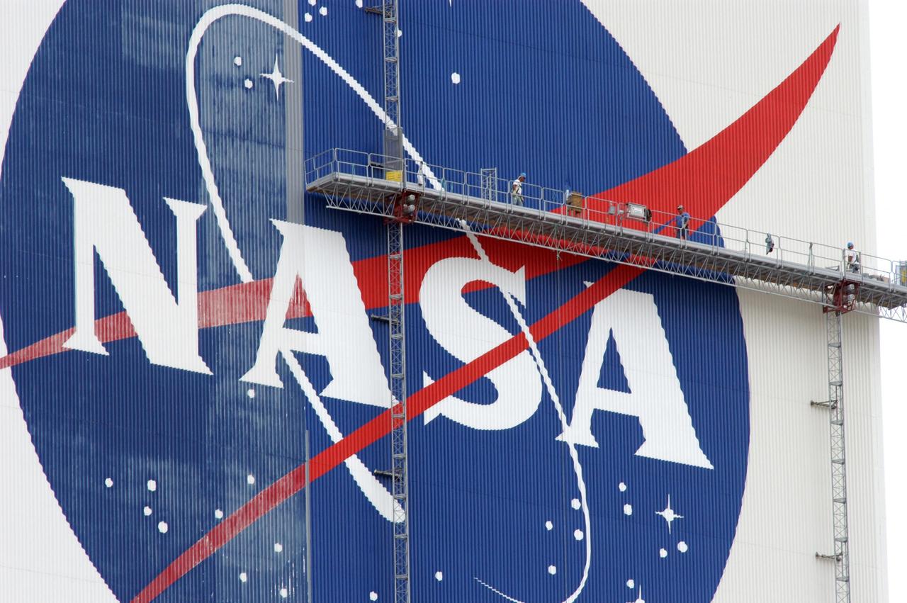 KENNEDY SPACE CENTER, FLA. --  On platforms suspended from the top of the 525-foot-high VAB, workers use rollers and brushes to repaint the U.S. flag on the southwest side of the Vehicle Assembly Building.   The flag spans an area 209 feet by 110 feet, or about 23, 437 square feet. Each stripe is 9 feet wide and each star is 6 feet in diameter. The logo is also being painted.  Known as the "meatball," the logo measures 110 feet by 132 feet, or about 12,300 square feet.  The flag and logo were last painted in 1998, honoring NASA's 40th anniversary.  Photo credit: NASA/George Shelton
