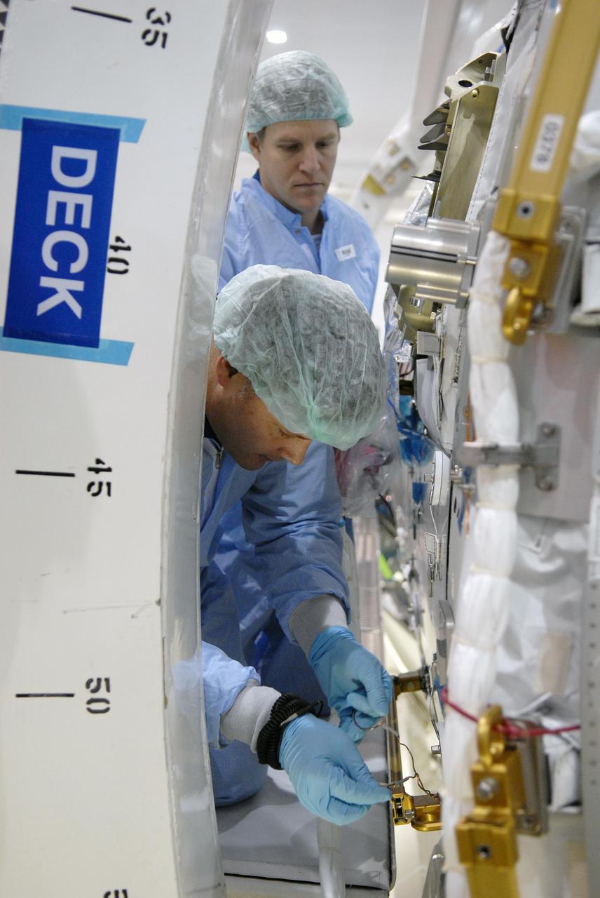 KENNEDY SPACE CENTER, FLA. -- STS-120 Mission Specialist Scott Parazynski (background) watches Mission Specialist Doug Wheelock work with a wire on the primary payload for the mission: the U.S. Node 2, another element to be added to the International Space Station. Parazynski, Wheelock and other crew members are familiarizing themselves with the payload. Node 2 will provide a passageway between three station science experiment facilities: the U.S. Destiny Laboratory, the Kibo Japanese Experiment Module, and the European Columbus Laboratory. STS-120 is targeted for launch on Sept. 7 with a crew of six, including Commander Pam Melroy, Pilot George Zamka, and Mission Specialist Mike Foreman. Photo credit: NASA/Kim Shiflett