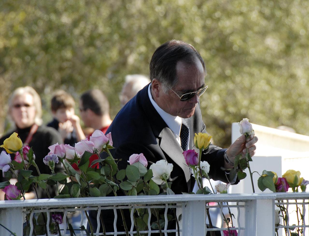 KENNEDY SPACE CENTER, FLA. -- Former astronaut Bob Crippen places a rose in the fence surrounding the Space Mirror Memorial at the KSC Visitor Complex. The Space Mirror was designated as a national memorial by Congress and President George Bush in 1991 to honor fallen astronauts. Their names are emblazoned on the monument's 42-1/2-foot-high by 50-foot-wide black granite surface as if to be projected into the heavens. Photo credit:NASA/Kim Shiflett