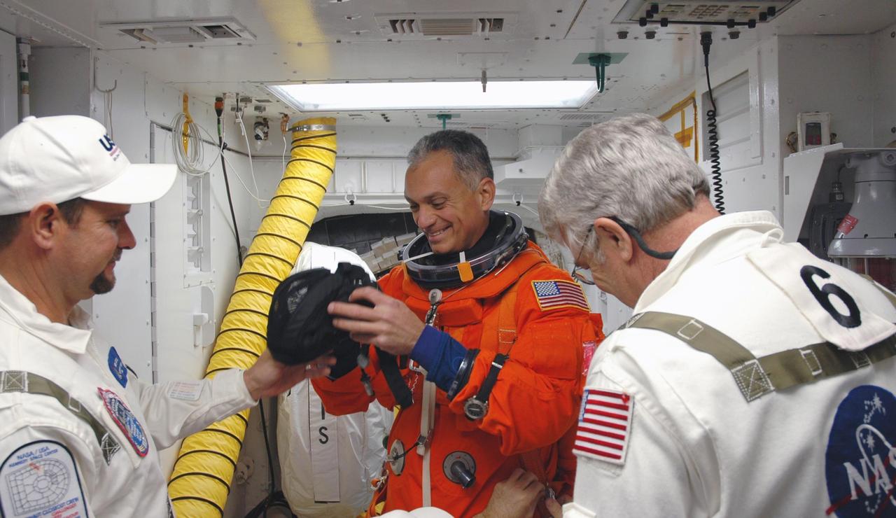 KENNEDY SPACE CENTER, FLA. -- In the white room on Launch Pad 39A, Mission STS-117 Mission Specialist Danny Olivas is helped with his gear before entering Space Shuttle Atlantis. The STS-117 crew practices for launch with a simulation of activities, from suit-up to countdown in the orbiter during terminal countdown demonstration test activities. The STS-117 mission is No. 21 to the International Space Station. Mission payloads aboard Atlantis include the S3/S4 integrated truss structure, a third set of solar arrays and batteries. The crew of six astronauts will install the truss to continue assembly of the station. Launch is scheduled for no earlier than March 15. Photo credit: NASA/Jim Grossmann