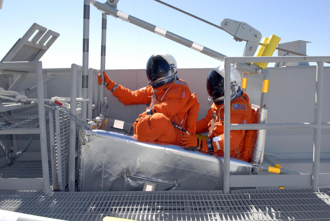 KENNEDY SPACE CENTER, FLA. --  From the 195-foot level of the fixed service structure on Launch Pad 39A, STS-117 Mission Specialists Danny Olivas (front) and James Reilly sit in a slidewire basket, part of the emergency egress system. They and other crew members are practicing the emergency egress procedure to get off the pad, part of the prelaunch preparations known as terminal countdown demonstration test (TCDT). The TCDT also includes M-113 armored personnel carrier training and payload familiarization. The STS-117 mission is No. 21 to the International Space Station. Mission payloads aboard Atlantis include the S3/S4 integrated truss structure, a third set of solar arrays and batteries. The crew of six astronauts will install the truss to continue assembly of the station. Launch is scheduled for no earlier than March 15.   Photo credit: NASA/Kim Shiflett.