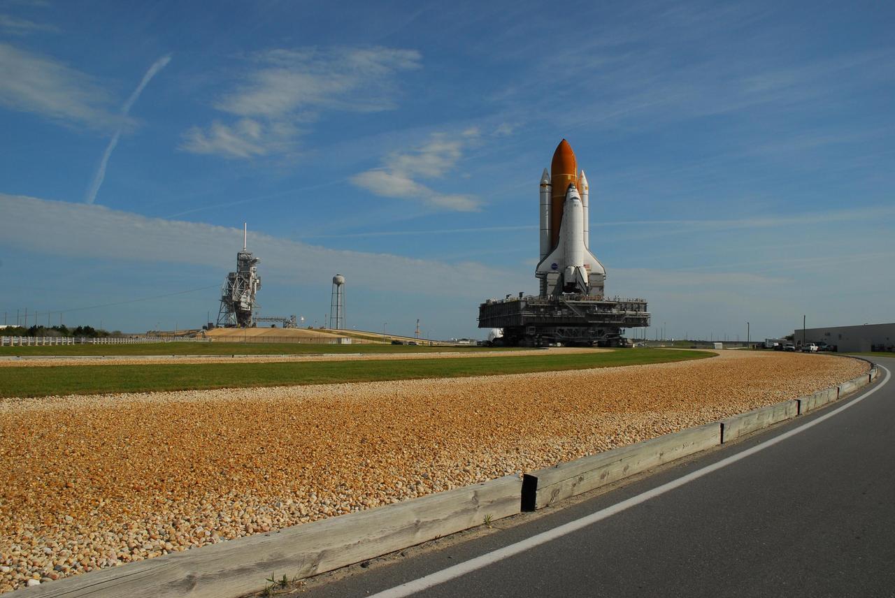 KENNEDY SPACE CENTER, FLA. --  Under a nearly clear blue sky, Space Shuttle Atlantis maneuvers the curve on the crawlerway as it heads back to the Vehicle Assembly Building from Launch Pad 39A (in the background, left).  In the VAB, the shuttle will be examined for hail damage. A severe thunderstorm with golf ball-sized hail caused divots in the giant tank's foam insulation and minor surface damage to about 26 heat shield tiles on the shuttle's left wing. Further evaluation of the tank is necessary to get an accurate accounting of foam damage and determine the type of repair required and the time needed for that work.  A new target launch date has not been determined, but teams will focus on preparing Atlantis for liftoff in late April.  Photo credit: NASA/Amanda Diller