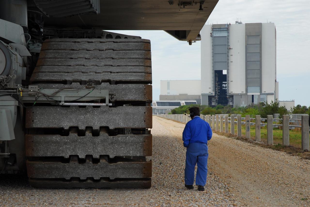 KENNEDY SPACE CENTER, FLA. --  A worker walks alongside the massive treads of the crawler-transporter that is moving Space Shuttle Atlantis back to the Vehicle Assembly Building, at right.  In the VAB, the shuttle will be examined for hail damage.  A severe thunderstorm with golf ball-sized hail caused divots in the giant tank's foam insulation and minor surface damage to about 26 heat shield tiles on the shuttle's left wing. Further evaluation of the tank is necessary to get an accurate accounting of foam damage and determine the type of repair required and the time needed for that work.  A new target launch date has not been determined, but teams will focus on preparing Atlantis for liftoff in late April.  Photo credit: NASA/Amanda Diller