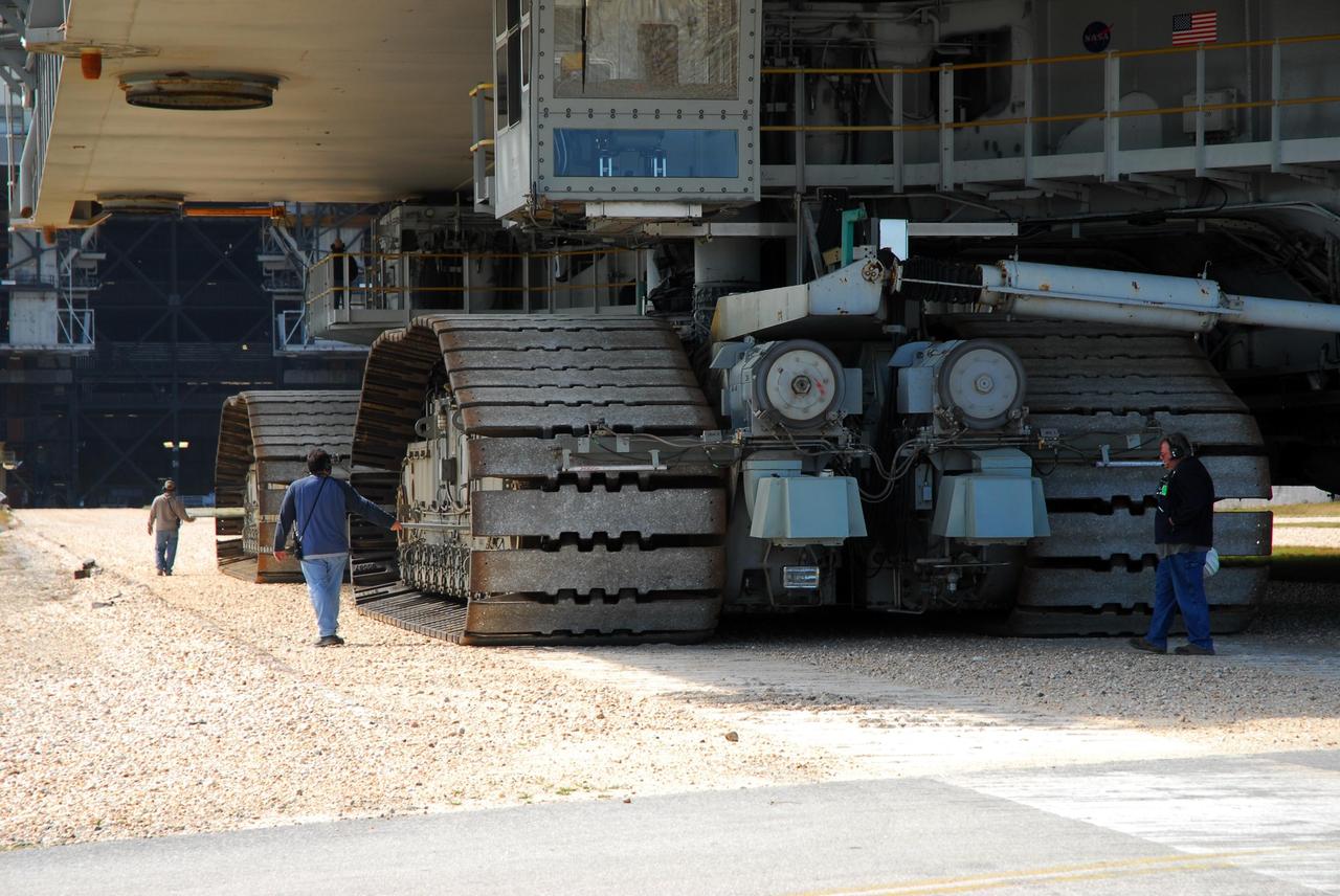KENNEDY SPACE CENTER, FLA. --  Workers stride alongside the massive treads of the crawler-transporter, which is moving Space Shuttle Atlantis, atop the mobile launcher platform, to the Vehicle Assembly Building.  In the VAB, the shuttle will be examined for hail damage.  A severe thunderstorm with golf ball-sized hail caused divots in the giant tank's foam insulation and minor surface damage to about 26 heat shield tiles on the shuttle's left wing. Further evaluation of the tank is necessary to get an accurate accounting of foam damage and determine the type of repair required and the time needed for that work.  A new target launch date has not been determined, but teams will focus on preparing Atlantis for liftoff in late April.  Photo credit: NASA/Amanda Diller