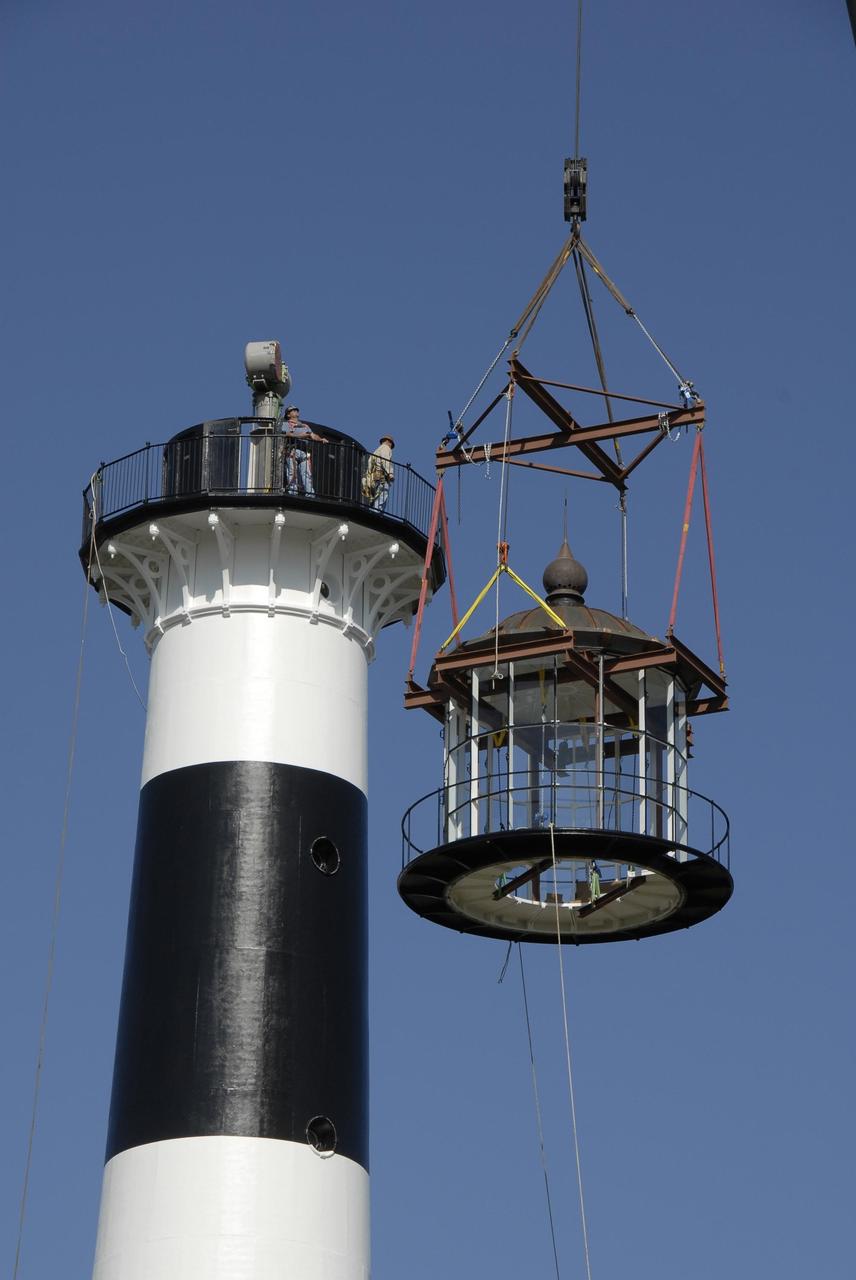 KENNEDY SPACE CENTER, FLA. --  A crane lifts a refurbished lantern to place on top of the Cape Canaveral Lighthouse, capping more than a year's work toward a $1 million restoration of the 150-year-old beacon.  The work included sandblasting the metal shell and filling the corrosion pits with epoxy, refurbishing the balcony and repairing the lantern.  To further the restoration, the Cape Canaveral Lighthouse Foundation plans to rebuild the lighthouse keeper's quarters from the original plans, as well as establish space for its archives and develop a meeting place.  The only lighthouse in the nation operated by the Air Force, it began guiding mariners in 1868.  An encroaching sea caused it to be moved inland and it was re-lighted in 1894 at its present location. The refurbishment was sponsored by the U.S. Air Force 45th Space Wing, whose officials said they wanted to help preserve the area's history.  The original brass roof, which had been in storage since its removal years ago, has been restored and once again tops the lighthouse.  As it is an active aid to navigation, the U.S. Coast Guard continues to be responsible for the optic, or light, which has a range of up to 22 nautical miles.  Photo credit: NASA/Kim Shiflett