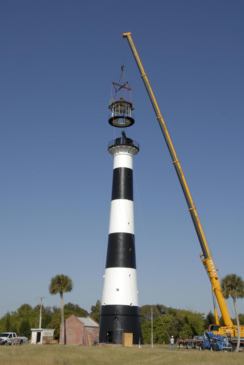 KENNEDY SPACE CENTER, FLA. --   A crane begins lowering a refurbished lantern on top of the Cape Canaveral Lighthouse, capping more than a year's work toward restoration of the 150-year-old beacon. The work included sandblasting the metal shell and filling the corrosion pits with epoxy, refurbishing the balcony and repairing the lantern. To further the restoration, the Cape Canaveral Lighthouse Foundation plans to rebuild the lighthouse keeper's quarters from the original plans, as well as establish space for its archives and develop a meeting place. The only lighthouse in the nation operated by the Air Force, it began guiding mariners in 1868. An encroaching sea caused it to be moved inland and it was re-lighted in 1894 at its present location. The refurbishment was sponsored by the U.S. Air Force 45th Space Wing, whose officials said they wanted to help preserve the area's history. The original brass roof, which had been in storage since its removal years ago, has been restored and once again tops the lighthouse. As it is an active aid to navigation, the U.S. Coast Guard continues to be responsible for the optic, or light, which has a range of up to 22 nautical miles. Photo credit: NASA/Kim Shiflett