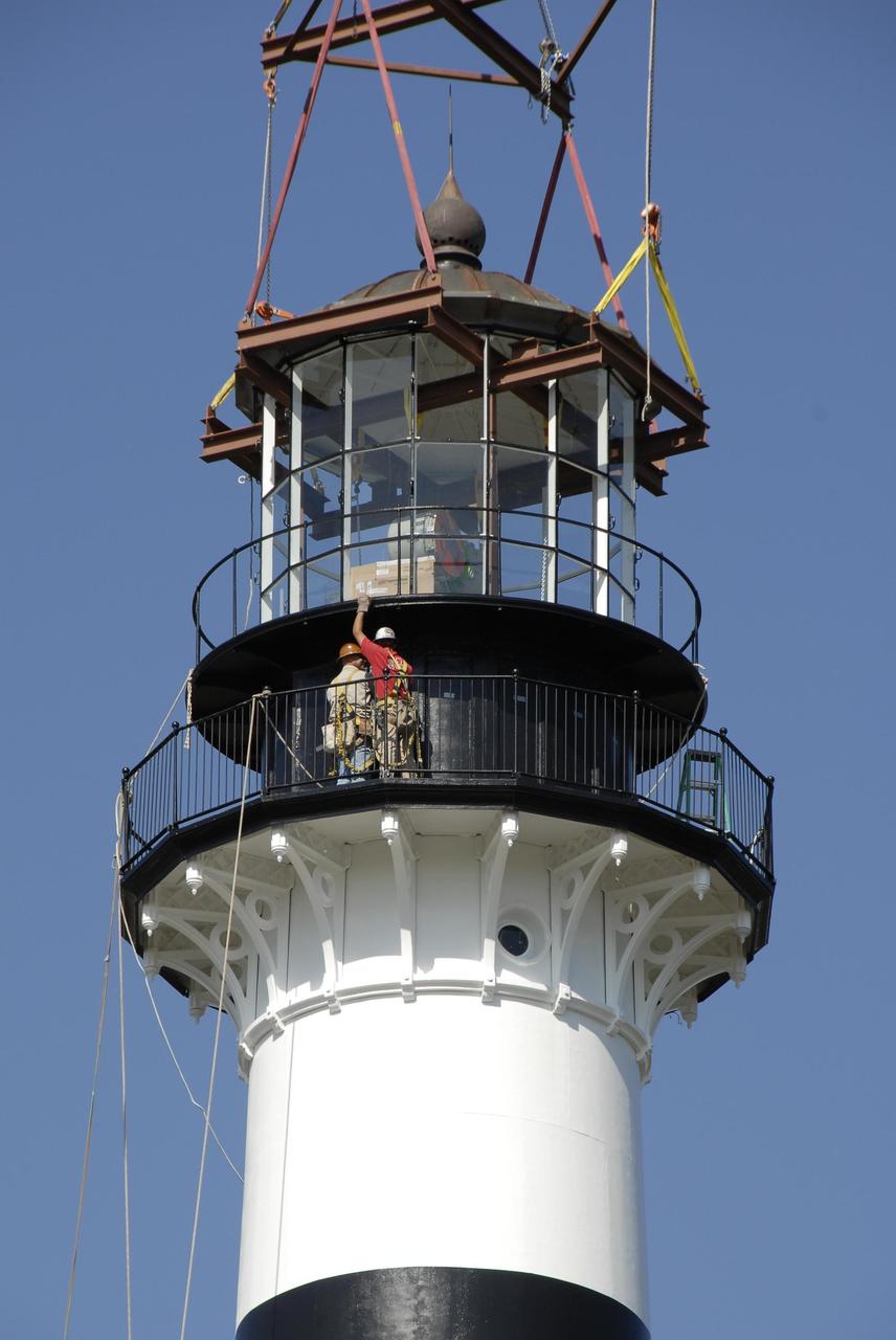 KENNEDY SPACE CENTER, FLA. --   Workers help guide a refurbished lantern on top of the Cape Canaveral Lighthouse, capping more than a year's work toward restoration of the 150-year-old beacon.  The work included sandblasting the metal shell and filling the corrosion pits with epoxy, refurbishing the balcony and repairing the lantern.  To further the restoration, the Cape Canaveral Lighthouse Foundation plans to rebuild the lighthouse keeper's quarters from the original plans, as well as establish space for its archives and develop a meeting place.  The only lighthouse in the nation operated by the Air Force, it began guiding mariners in 1868.  An encroaching sea caused it to be moved inland and it was re-lighted in 1894 at its present location. The refurbishment was sponsored by the U.S. Air Force 45th Space Wing, whose officials said they wanted to help preserve the area's history.  The original brass roof, which had been in storage since its removal years ago, has been restored and once again tops the lighthouse.  As it is an active aid to navigation, the U.S. Coast Guard continues to be responsible for the optic, or light, which has a range of up to 22 nautical miles.  Photo credit: NASA/Kim Shiflett