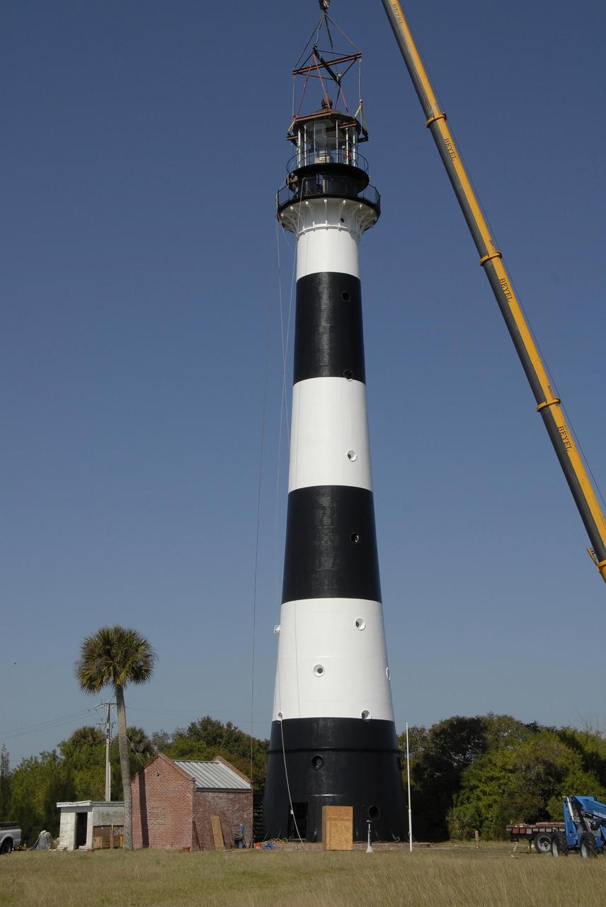 KENNEDY SPACE CENTER, FLA. --   A crane lowers a refurbished lantern on top of the Cape Canaveral Lighthouse, capping more than a year's work toward restoration of the 150-year-old beacon.   The work included sandblasting the metal shell and filling the corrosion pits with epoxy, refurbishing the balcony and repairing the lantern.  To further the restoration, the Cape Canaveral Lighthouse Foundation plans to rebuild the lighthouse keeper's quarters from the original plans, as well as establish space for its archives and develop a meeting place.  The only lighthouse in the nation operated by the Air Force, it began guiding mariners in 1868.  An encroaching sea caused it to be moved inland and it was re-lighted in 1894 at its present location. The refurbishment was sponsored by the U.S. Air Force 45th Space Wing, whose officials said they wanted to help preserve the area's history.  The original brass roof, which had been in storage since its removal years ago, has been restored and once again tops the lighthouse.  As it is an active aid to navigation, the U.S. Coast Guard continues to be responsible for the optic, or light, which has a range of up to 22 nautical miles.  Photo credit: NASA/Kim Shiflett