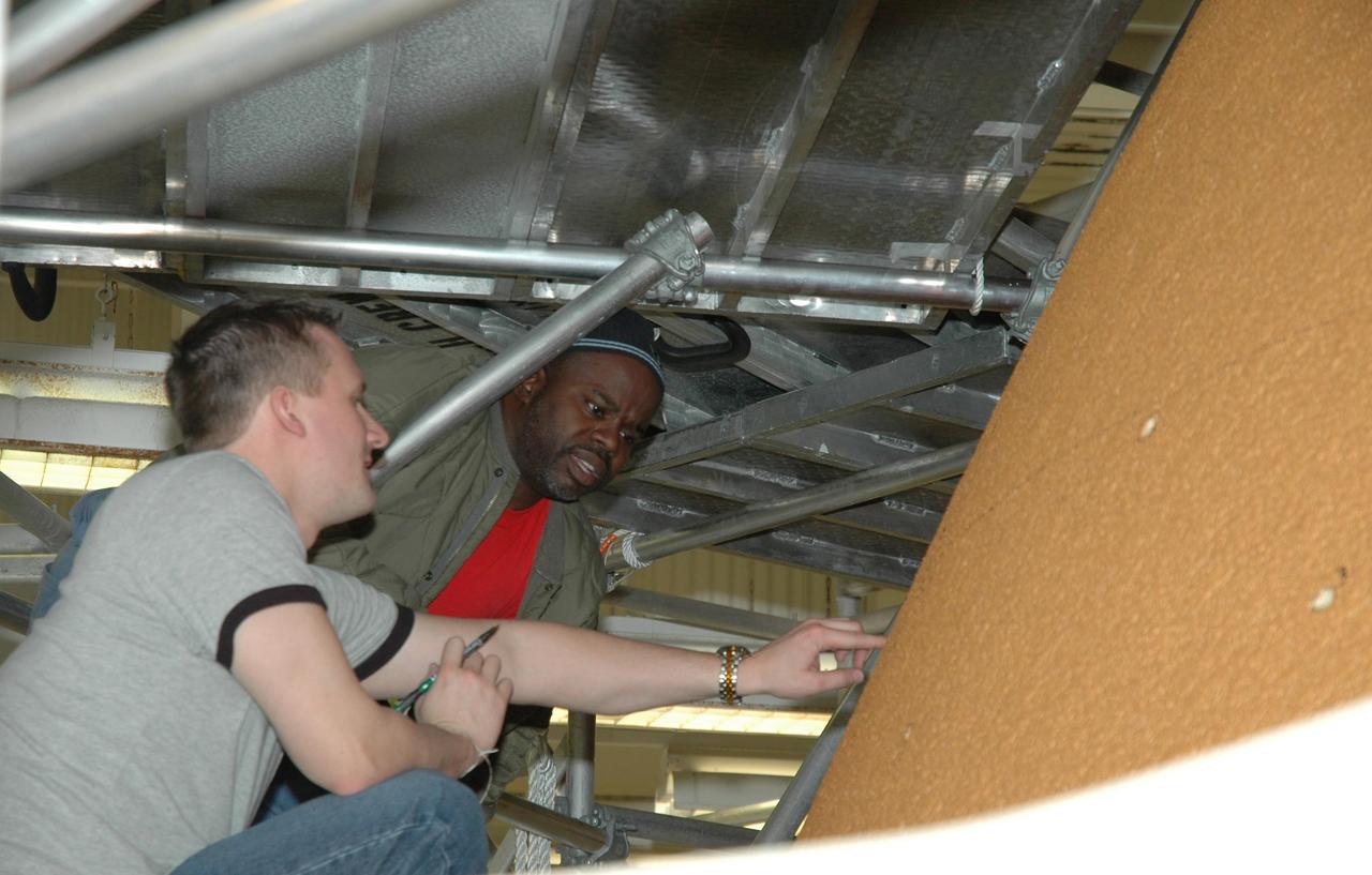 KENNEDY SPACE CENTER, FLA. -- In Highbay 1 inside the Vehicle Assembly Building, technicians look at hail damage on the external tank. A severe thunderstorm with golf ball-sized hail caused visible divots in the giant tank's foam insulation and minor surface damage to about 26 heat shield tiles on the shuttle's left wing. A new target launch date has not been determined, but teams will focus on preparing Atlantis for liftoff in late April on mission STS-117. Photo credit: NASA/Jim Grossmann