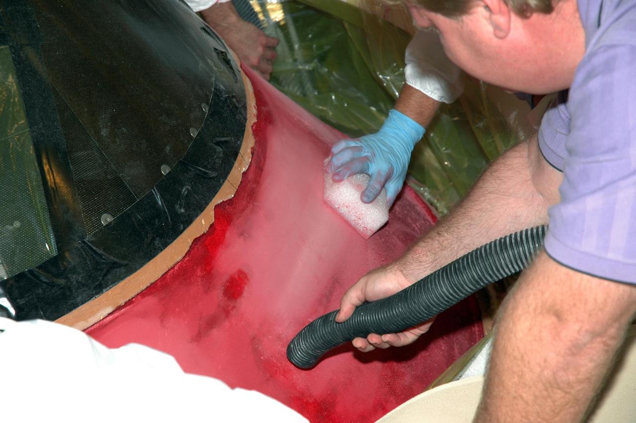 KENNEDY SPACE CENTER, FLA. -- In Highbay 1 inside the Vehicle Assembly Building, a technician carefully sands away the red dye that has been applied to the external tank to help expose cracks or compression dents, while another technician uses a compression hose to remove excess particles.  A severe thunderstorm with golf ball-sized hail caused visible divots in the giant tank's foam insulation and minor surface damage to about 26 heat shield tiles on the shuttle's left wing. A new target launch date has not been determined, but teams will focus on preparing Atlantis for liftoff in late April on mission STS-117. Photo credit: NASA/Jim Grossmann