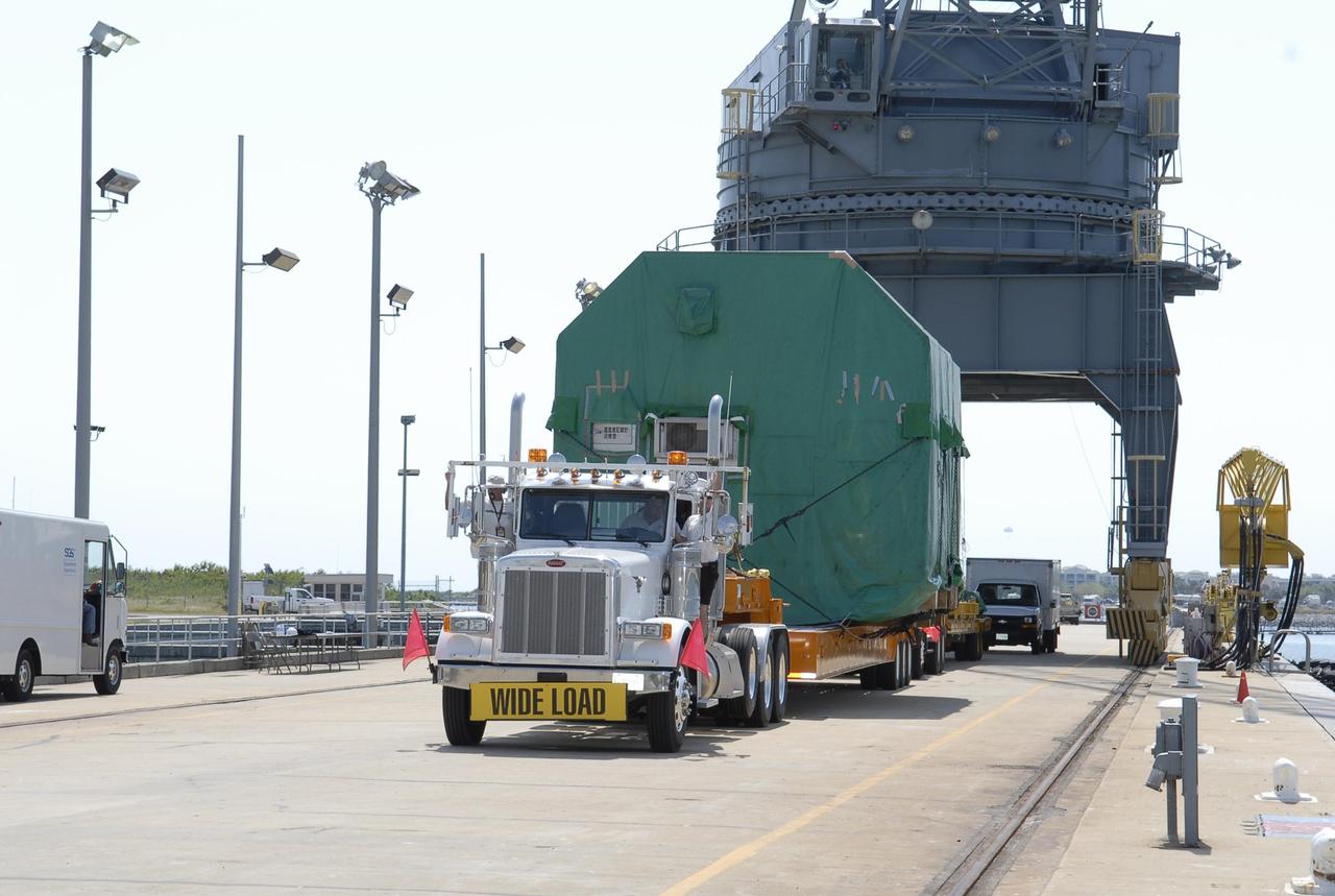 KENNEDY SPACE CENTER, FLA. -- A flat bed truck hauls the container with the Experiment Logistics Module Pressurized Section inside away from the Trident wharf. The logistics module is part of the Japanese Experiment Module. The logistics module is being transported to the Space Station Processing Facility at NASA's Kennedy Space Center. The Japanese Experiment Module is composed of three segments and is known as Kibo, which means "hope" in Japanese. Kibo consists of six components: two research facilities -- the Pressurized Module and Exposed Facility; a Logistics Module attached to each of them; a Remote Manipulator System; and an Inter-Orbit Communication System unit. Kibo also has a scientific airlock through which experiments are transferred and exposed to the external environment of space. Kibo is Japan's first human space facility and its primary contribution to the station. Kibo will enhance the unique research capabilities of the orbiting complex by providing an additional environment in which astronauts can conduct science experiments. The various components of JEM will be assembled in space over the course of three Space Shuttle missions. The first of those three missions, STS-123, will carry the Experiment Logistics Module Pressurized Section aboard the Space Shuttle Endeavour, targeted for launch in 2007. Photo credit: NASA/Kim Shiflett