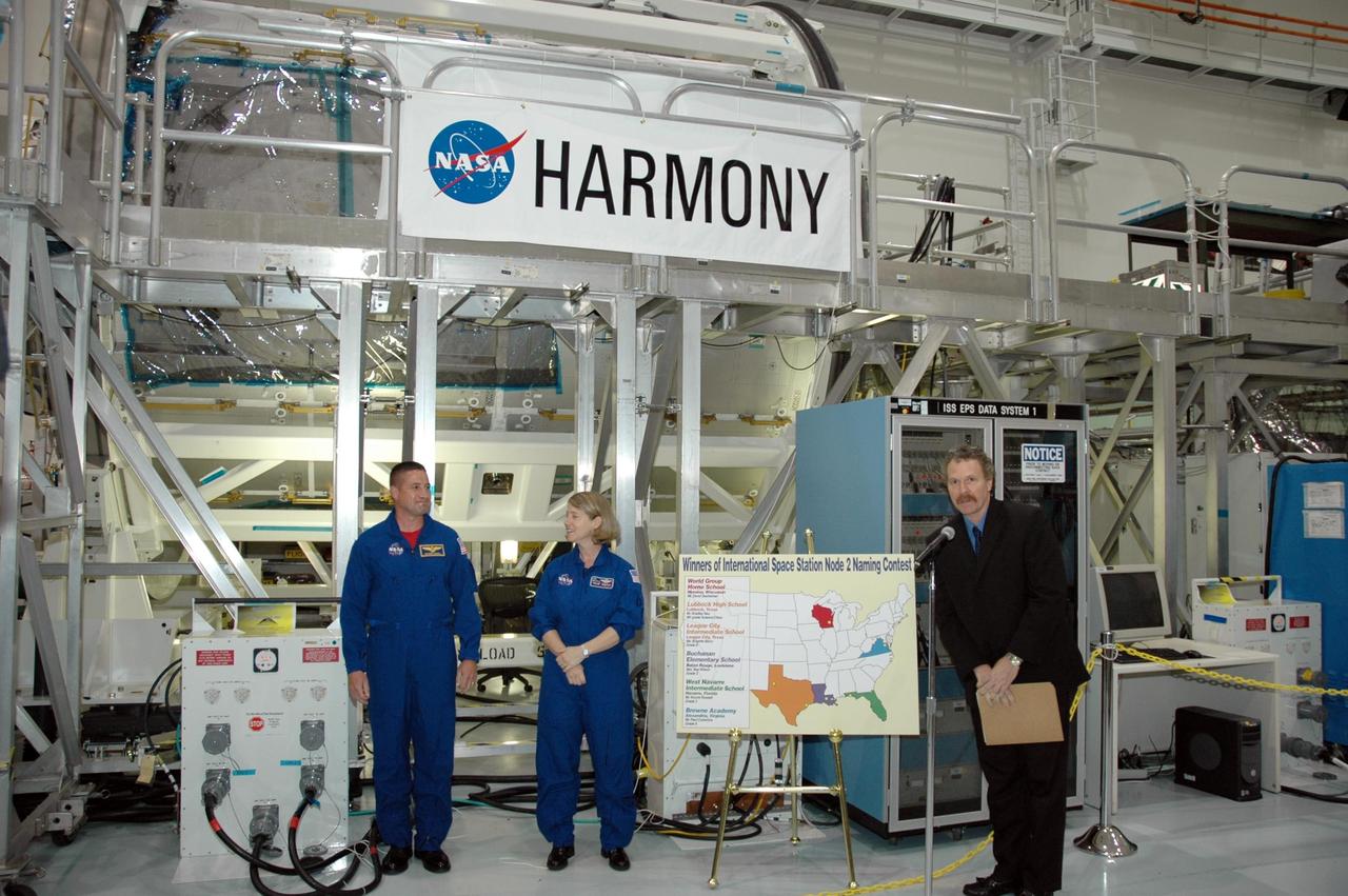 KENNEDY SPACE CENTER, FLA. -- In the Space Station Processing Facility, Mission STS-120 Pilot George Zamka (left) and Commander Pam Melroy stand in front of the Node 2 module with it's new name, Harmony, unveiled, as Russ Romanella, director of International Space Station and Spacecraft Processing presides over the ceremony. The name, Harmony, was chosen from an academic competition involving thousands of students in kindergarten through high school. The Node 2 Challenge required students to learn about the International Space Station, build a scale model of the module, and write an essay explaining their proposed name. This will be the first U.S. piece of the space station named by someone other than a NASA official. Node 2 is a pressurized module that will act as a connecting port and passageway to additional international science labs and supply spacecraft. It also will be a work platform for the station's robotic arm. The module is scheduled to fly on mission STS-120 aboard Space Shuttle Atlantis targeted for later this year. Photo credit: NASA/Jim Grossmann