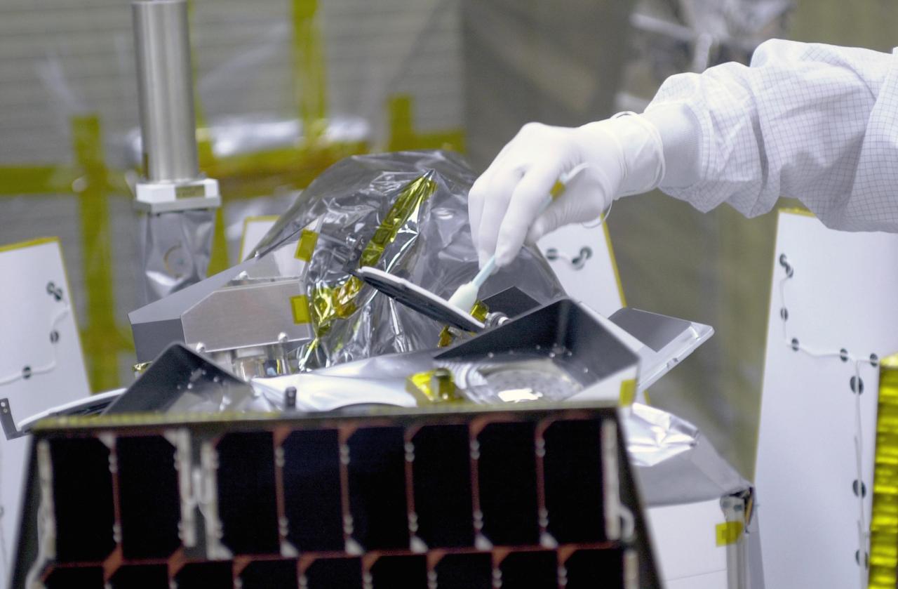 VANDENBERG AIR FORCE BASE, CALIF. -- In a clean-room environment at North Vandenberg Air Force Base, technicians remove covers from instruments in the AIM spacecraft while solar panels are partially deployed. AIM will fly three instruments designed to study polar mesospheric clouds located at the edge of space, 50 miles above the Earth's surface in the coldest part of the planet's atmosphere. The mission's primary goal is to explain why these clouds form and what has caused them to become brighter and more numerous and appear at lower latitudes in recent years. AIM's results will provide the basis for the study of long-term variability in the mesospheric climate and its relationship to global climate change. AIM is scheduled to be mated to the Pegasus XL during the second week of April, after which final inspections will be conducted. Launch is scheduled for April 25.