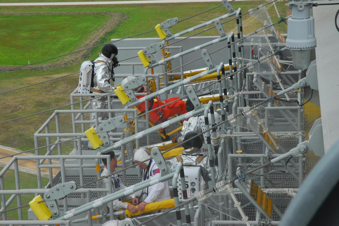 KENNEDY SPACE CENTER, FLA.  -- During a simulated rescue mission on Launch Pad 39A, known as Mode 2,  KSC workers dressed in astronauts' launch-and-entry suits are climbing into the slidewire baskets.  A fire rescue team is simulating extracting the crew from the orbiter and helping them to the baskets.The KSC rescue teams are practicing emergency procedures in the unlikely scenario of a mishap on the pad during a launch sequence.  The exercises are standard training procedures to assess and prepare emergency personnel, procedures and hardware.  Photo credit: NASA/Jack Pfaller