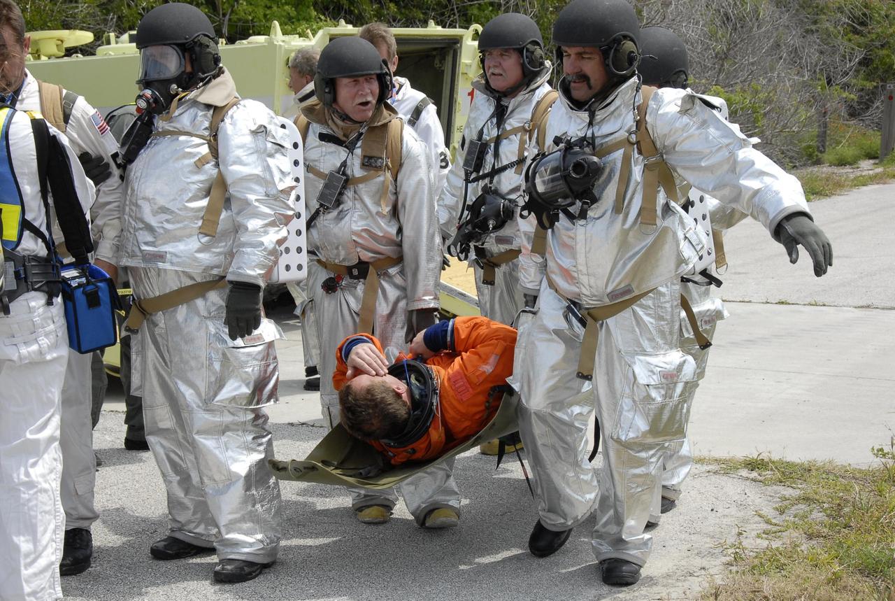 KENNEDY SPACE CENTER, FLA. -- During the second stage of a simulated emergency, known as Mode 4, a KSC rescue team carries a worker portraying an "injured" astronaut toward the triage area set up at Helipad 8, located near the fire station between Launch Pads 39A and 39B. The emergency exercise began on Launch Pad 39A. The participants were helped off the pad and taken to the triage site. The "injured" workers will be airlifted to participating area hospitals. The KSC rescue teams are practicing emergency procedures in the unlikely scenario of a mishap on the pad during a launch sequence. The exercises are standard training procedures to assess and prepare emergency personnel, procedures and hardware. Photo credit: NASA/Kim Shiflett