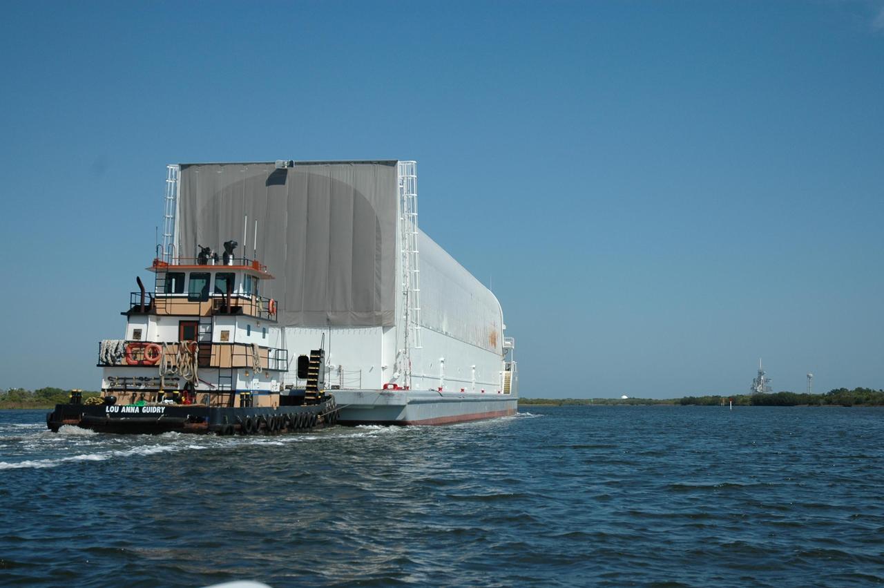 KENNEDY SPACE CENTER, FLA. -- The Pegasus barge is towed on the barge channel leading to the Launch Complex 39 Area. The barge's cargo is the external tank prepared for mission STS-118 by the Michoud Assembly Facility near New Orleans. Visible at right is one of the launch pads and the nearby water tower. The destination of the barge is the turn basin near the Vehicle Assembly Building where the tank will be offloaded and moved to the VAB. Photo credit: Dimitri Gerondidakis