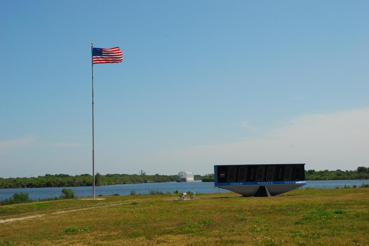 KENNEDY SPACE CENTER, FLA.  --  The Pegasus barge is towed into the turn basin in the Launch Complex 39 Area.  In the foreground are the U.S. flag and launch countdown clock near the NASA News Center. The barge's cargo is the external tank prepared for mission STS-118 by the Michoud Assembly Facility near New Orleans.  After docking, the tank will eventually be offloaded and moved to the Vehicle Assembly Building..  Photo credit: Jack Pfaller