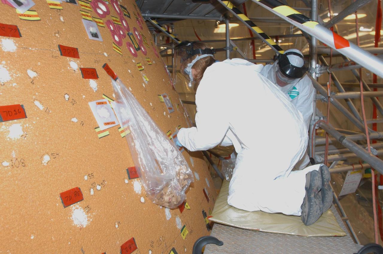 KENNEDY SPACE CENTER, FLA.  -- In the Vehicle Assembly Building, United Space Alliance technicians Brenda Morris and Brian Williams are applying foam and molds on Space Shuttle Atlantis' external tank to areas damaged by hail.  The white hole with a red circle around it  (upper right) is a hole prepared for molding and material application. The red material is sealant tape so the mold doesn't leak when the foam rises against the mold. The white/translucent square mold is an area where the foam has been applied and the foam has risen and cured against the mold surface.   In late February, Atlantis' external tank received hail damage during a severe thunderstorm that passed through the Kennedy Space Center Launch Complex 39 area. The hail caused visible divots in the giant tank's foam insulation as well as minor surface damage to about 26 heat shield tiles on the shuttle's left wing.   The March launch was postponed and has not yet been rescheduled due to the repair process.  Photo credit: NASA/George Shelton