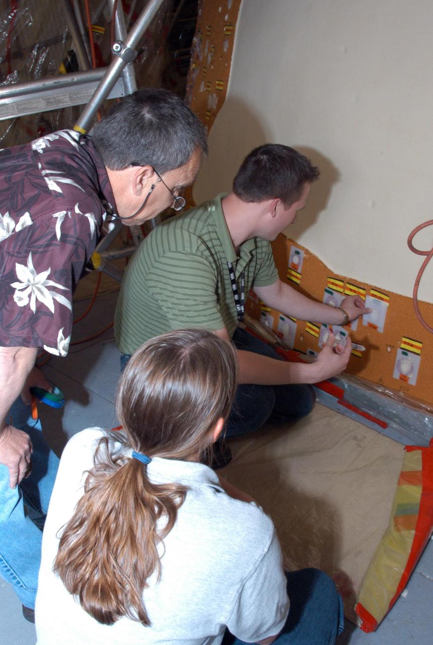 KENNEDY SPACE CENTER, FLA.  --   In the Vehicle Assembly Building, the repair work of hail damage on Atlantis' external tank is inspected.  At left is Brian Miller, with NASA Quality Assurance; at right is Mike Ravenscroft, with United Space Alliance.  In the front is Sabrena Yedo, with NASA Safety.  In late February, Atlantis' external tank received hail damage during a severe thunderstorm that passed through the Kennedy Space Center Launch Complex 39 area. The hail caused visible divots in the giant tank's foam insulation as well as minor surface damage to about 26 heat shield tiles on the shuttle's left wing.  The launch now is targeted for June 8.  Photo credit: NASA/George Shelton