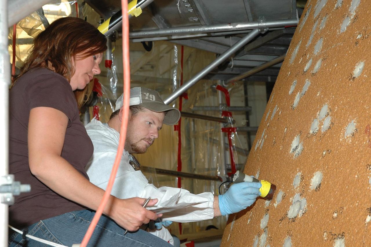 KENNEDY SPACE CENTER, FLA.  --  In the Vehicle Assembly Building, workers check foam repairs on Atlantis' external tank.  In late February, Atlantis' external tank received hail damage during a severe thunderstorm that passed through the Kennedy Space Center Launch Complex 39 area. The hail caused visible divots in the giant tank's foam insulation as well as minor surface damage to about 26 heat shield tiles on the shuttle's left wing.  The launch now is targeted for June 8.   Photo credit: NASA/Jack Pfaller
