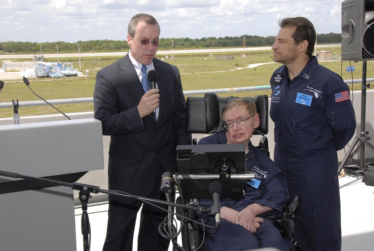 KENNEDY SPACE CENTER, FLA. -- At the Kennedy Space Center Shuttle Landing Facility, Space Florida president Steve Kohler (left) talks to the media about physicist Stephen Hawking's (in the wheelchair) first zero-gravity flight. The flight will be aboard a modified Boeing 727 aircraft owned by Zero Gravity Corp., a commercial company licensed to provide the public with weightless flight experiences.  At right is Peter Diamandis, founder of the Zero Gravity Corp.  Hawking developed amyotrophic lateral sclerosis disease in the 1960s, a type of motor neuron disease which would cost him the loss of almost all neuromuscular control. At the celebration of his 65th birthday on January 8 this year, Hawking announced his plans for a zero-gravity flight to prepare for a sub-orbital space flight in 2009 on Virgin Galactic's space service.  Photo credit: NASA/Kim Shiflett
