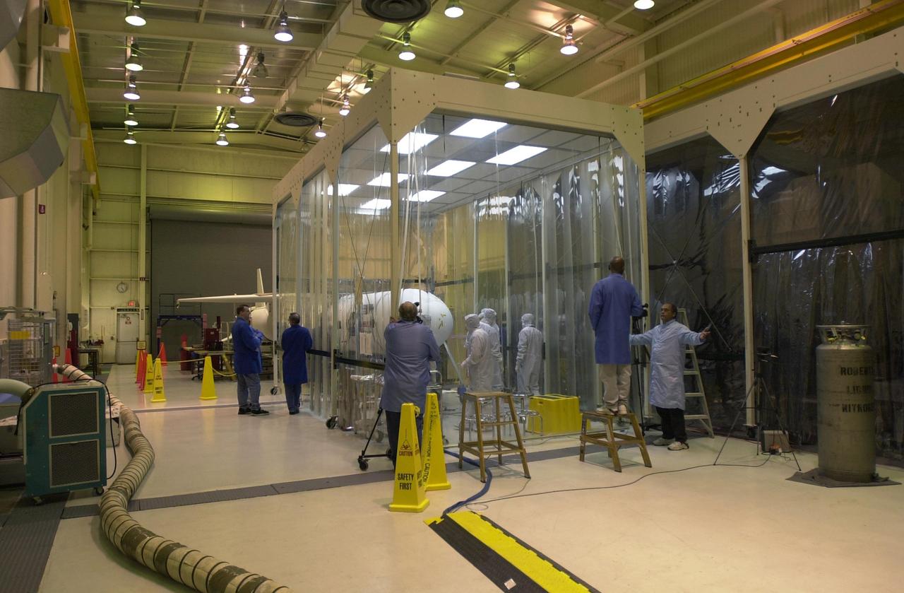 KENNEDY SPACE CENTER, FLA. -- At Vandenberg Air Force Base in California, under the protective clean tent, technicians examine the installation of the fairing around the AIM spacecraft. The fairing is a molded structure that fits around the spacecraft and forms an aerodynamically smooth nose cone, protecting the spacecraft during launch. Launch will be from a Pegasus XL rocket, carried and released by Orbital Sciences L-1011 jet aircraft. AIM, which stands for Aeronomy of Ice in the Mesosphere, is being prepared for integrated testing and a flight simulation. The AIM spacecraft will fly three instruments designed to study polar mesospheric clouds located at the edge of space, 50 miles above the Earth's surface in the coldest part of the planet's atmosphere. The mission's primary goal is to explain why these clouds form and what has caused them to become brighter and more numerous and appear at lower latitudes in recent years. AIM's results will provide the basis for the study of long-term variability in the mesospheric climate and its relationship to global climate change. Launch is scheduled for April 25.