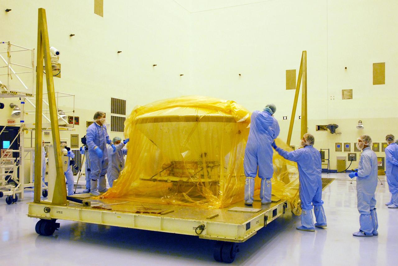 KENNEDY SPACE CENTER, FLA. --  In the Payload Hazardous Servicing Facility at Kennedy Space Center, workers dressed in clean-room garb begin removing the protective wrapping from around the Phoenix spacecraft. The Phoenix mission is the first project in NASA's first openly competed program of Mars Scout missions. Phoenix will land in icy soils near the north polar permanent ice cap of Mars and explore the history of the water in these soils and any associated rocks, while monitoring polar climate. Landing is planned in May 2008 on arctic ground where a mission currently in orbit, Mars Odyssey, has detected high concentrations of ice just beneath the top layer of soil. It will serve as NASA's first exploration of a potential modern habitat on Mars and open the door to a renewed search for carbon-bearing compounds, last attempted with NASA’s Viking missions in the 1970s. A stereo color camera and a weather station will study the surrounding environment while the other instruments check excavated soil samples for water, organic chemicals and conditions that could indicate whether the site was ever hospitable to life. Microscopes can reveal features as small as one one-thousandth the width of a human hair. Launch of Phoenix aboard a Delta II rocket is targeted for Aug. 3 from Cape Canaveral Air Force Station in Florida.  Photo credit: NASA/George Shelton