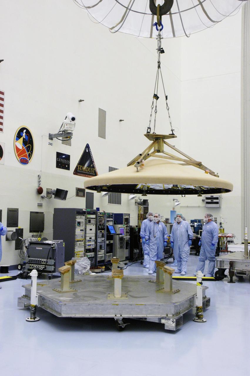 KENNEDY SPACE CENTER, FLA. --  In the Payload Hazardous Servicing Facility, workers watch as an overhead crane lowers the heat shield toward a platform. The heat shield was removed from the Phoenix Mars Lander spacecraft. The Phoenix mission is the first project in NASA's first openly competed program of Mars Scout missions. Phoenix will land in icy soils near the north polar permanent ice cap of Mars and explore the history of the water in these soils and any associated rocks, while monitoring polar climate. Landing is planned in May 2008 on arctic ground where a mission currently in orbit, Mars Odyssey, has detected high concentrations of ice just beneath the top layer of soil. It will serve as NASA's first exploration of a potential modern habitat on Mars and open the door to a renewed search for carbon-bearing compounds, last attempted with NASA’s Viking missions in the 1970s. A stereo color camera and a weather station will study the surrounding environment while the other instruments check excavated soil samples for water, organic chemicals and conditions that could indicate whether the site was ever hospitable to life. Microscopes can reveal features as small as one one-thousandth the width of a human hair. Launch of Phoenix aboard a Delta II rocket is targeted for Aug. 3 from Cape Canaveral Air Force Station in Florida.   Photo credit: NASA/George Shelton