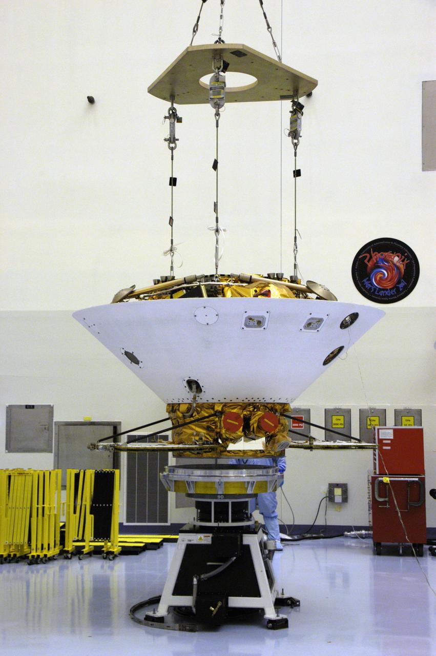 KENNEDY SPACE CENTER, FLA. -- An overhead crane lowers the backshell with the Phoenix Mars Lander inside onto a spin table for spin testing in the Payload Hazardous Servicing Facility. The Phoenix mission is the first project in NASA's first openly competed program of Mars Scout missions. Phoenix will land in icy soils near the north polar permanent ice cap of Mars and explore the history of the water in these soils and any associated rocks, while monitoring polar climate. Landing is planned in May 2008 on arctic ground where a mission currently in orbit, Mars Odyssey, has detected high concentrations of ice just beneath the top layer of soil. It will serve as NASA's first exploration of a potential modern habitat on Mars and open the door to a renewed search for carbon-bearing compounds, last attempted with NASA’s Viking missions in the 1970s. A stereo color camera and a weather station will study the surrounding environment while the other instruments check excavated soil samples for water, organic chemicals and conditions that could indicate whether the site was ever hospitable to life. Microscopes can reveal features as small as one one-thousandth the width of a human hair. Launch of Phoenix aboard a Delta II rocket is targeted for Aug. 3 from Cape Canaveral Air Force Station in Florida.   Photo credit: NASA/George Shelton