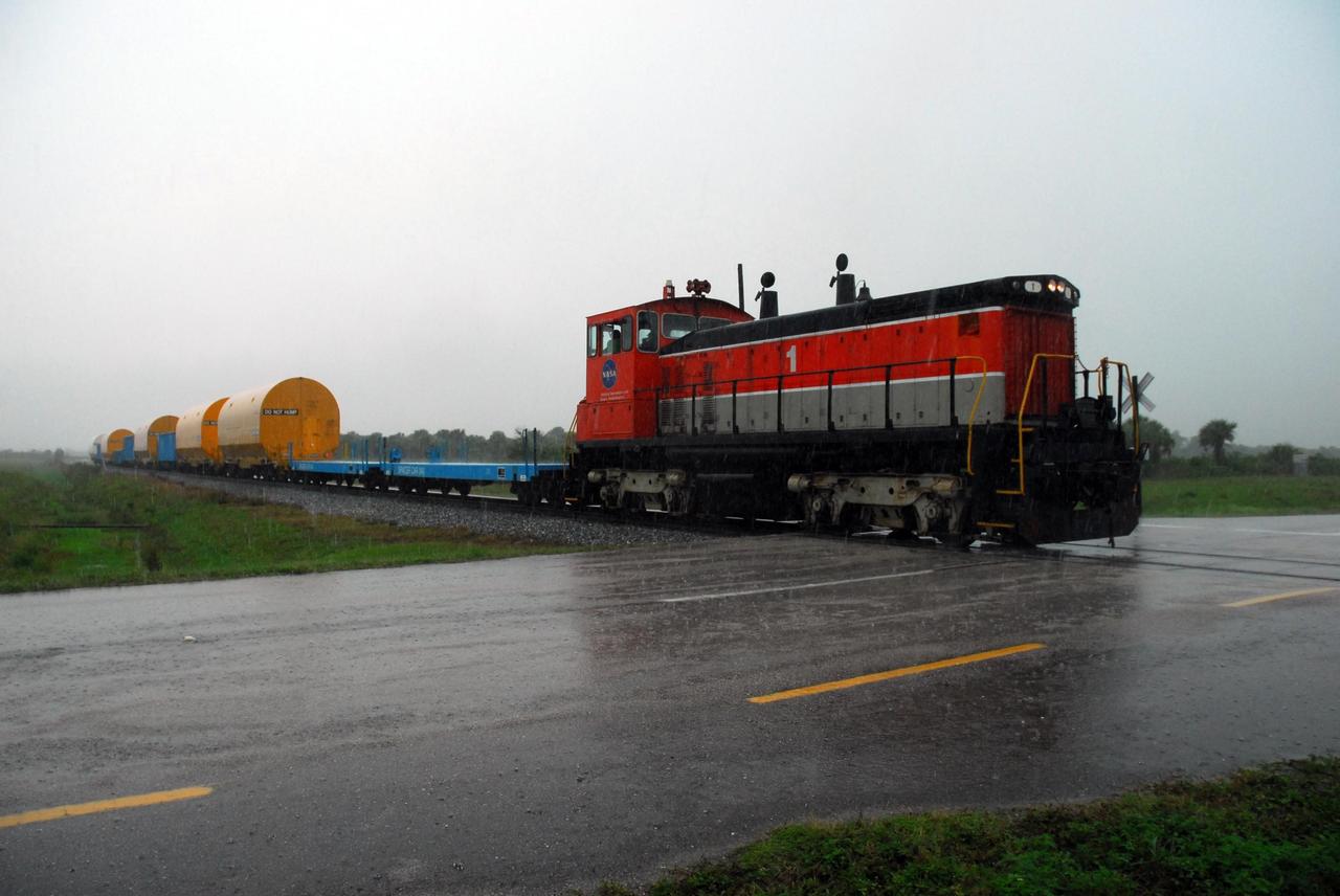 KENNEDY SPACE CENTER, FLA. --   The locomotive and rail cars carrying solid rocket booster motor segments and two aft exit cone segments cross a road on Kennedy Space Center.  These cars are headed for the SRB Assembly and Refurbishment Facility.  While enroute, solid rocket motor segments were involved in a derailment in Alabama.  The rail cars carrying these segments remained upright and were undamaged.  An inspection determined these segment cars could continue on to Florida.  The segments themselves will undergo further evaluation at Kennedy before they are cleared for flight.  Other segments involved in the derailment will be returned to a plant in Utah for further evaluation.  Photo credit: NASA/George Shelton