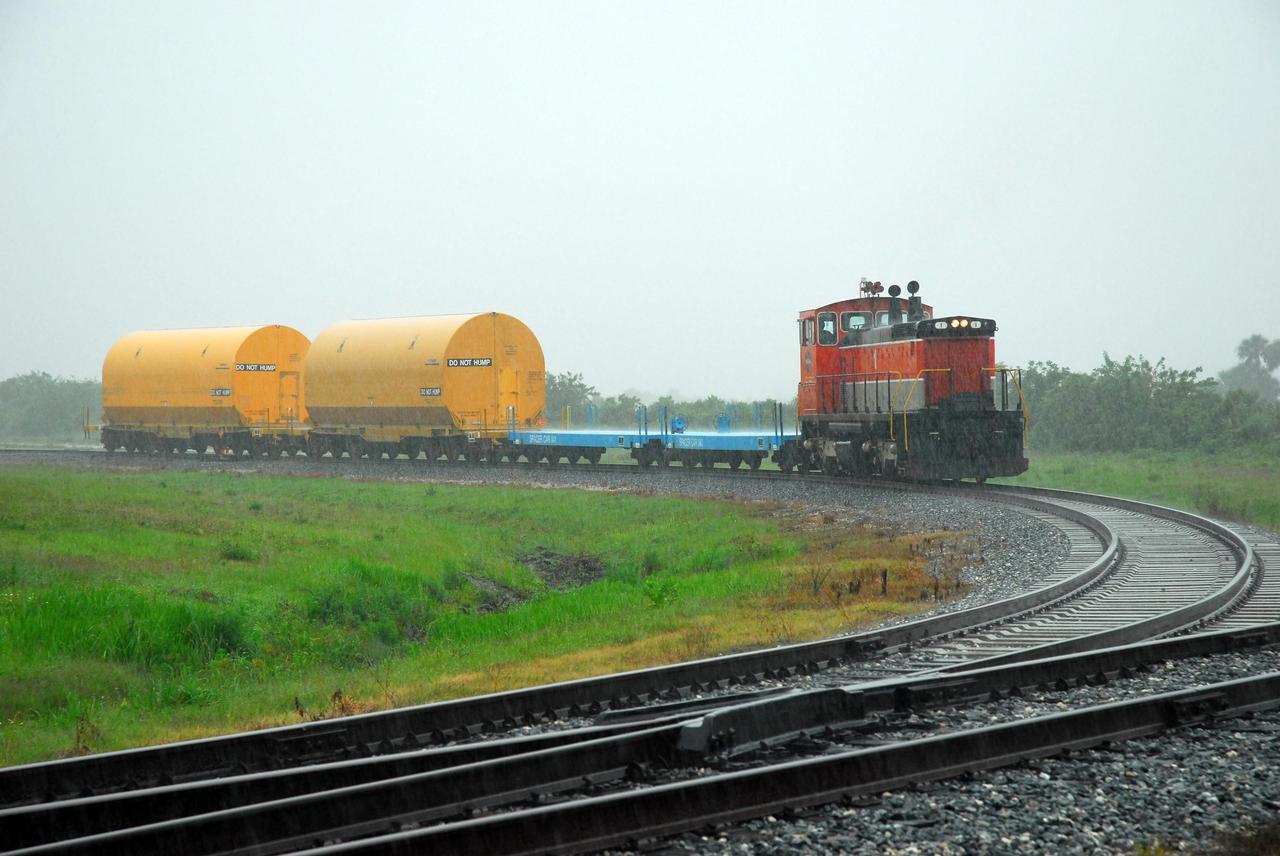 KENNEDY SPACE CENTER, FLA. --   The locomotive and rail cars carrying solid rocket booster motor segments and two aft exit cone segments cross a road on Kennedy Space Center.  These cars are headed for the SRB Assembly and Refurbishment Facility.   While enroute, solid rocket motor segments were involved in a derailment in Alabama.  The rail cars carrying these segments remained upright and were undamaged.  An inspection determined these segment cars could continue on to Florida.  The segments themselves will undergo further evaluation at Kennedy before they are cleared for flight.  Other segments involved in the derailment will be returned to a plant in Utah for further evaluation.  Photo credit: NASA/George Shelton