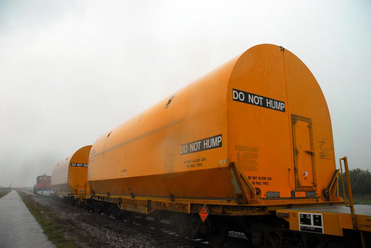 KENNEDY SPACE CENTER, FLA. -- The locomotive and rail cars carrying solid rocket booster motor segments and two aft exit cone segments cross a road on Kennedy Space Center. These cars are headed for the SRB Assembly and Refurbishment Facility. While enroute, solid rocket motor segments were involved in a derailment in Alabama. The rail cars carrying these segments remained upright and were undamaged. An inspection determined these segment cars could continue on to Florida. The segments themselves will undergo further evaluation at Kennedy before they are cleared for flight. Other segments involved in the derailment will be returned to a plant in Utah for further evaluation. Photo credit: NASA/George Shelton